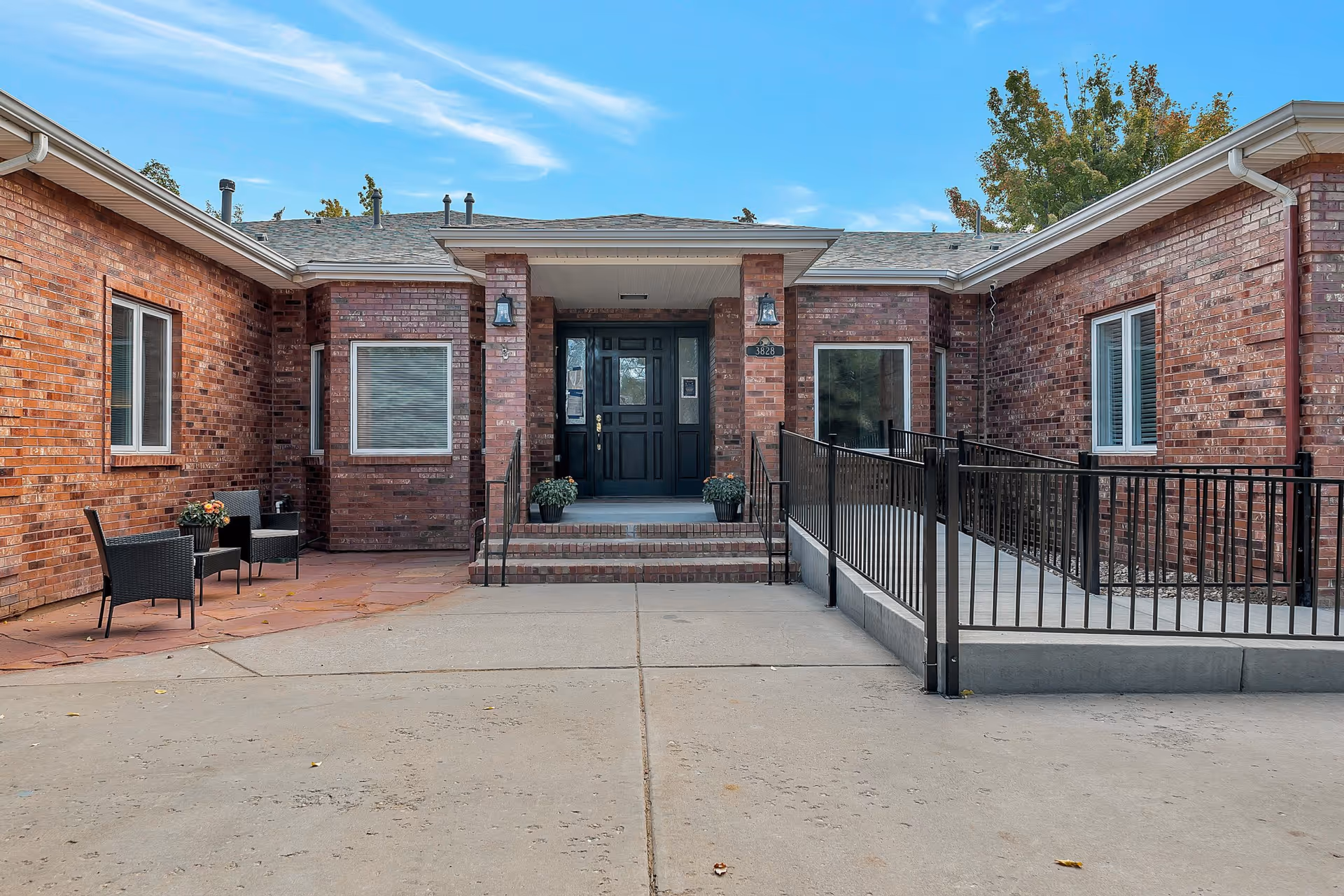 Brick building exterior with a central entrance, steps, ramp, and seating.