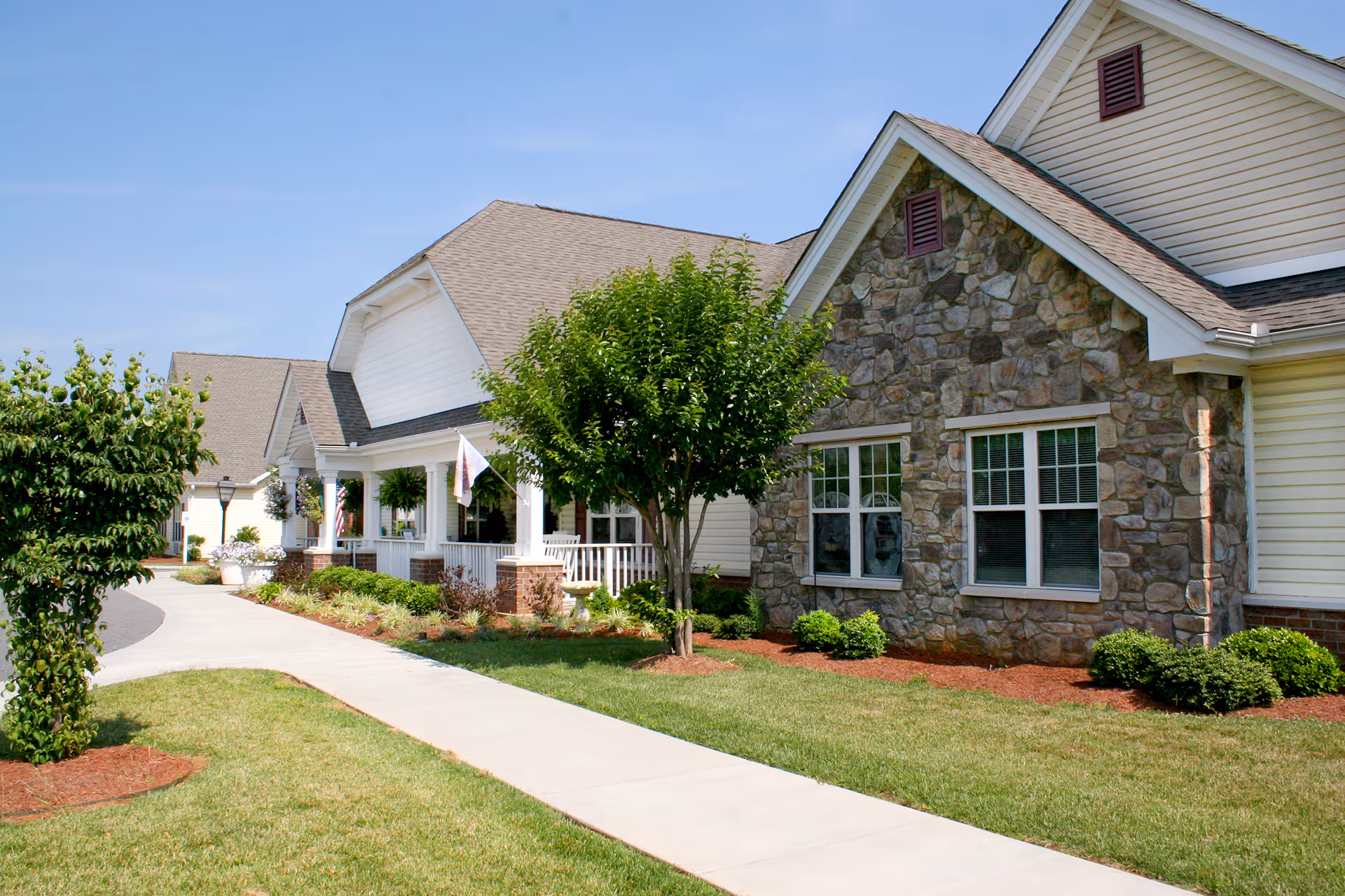 Exterior view of a senior living facility with stone facade, manicured lawn, and walkway.