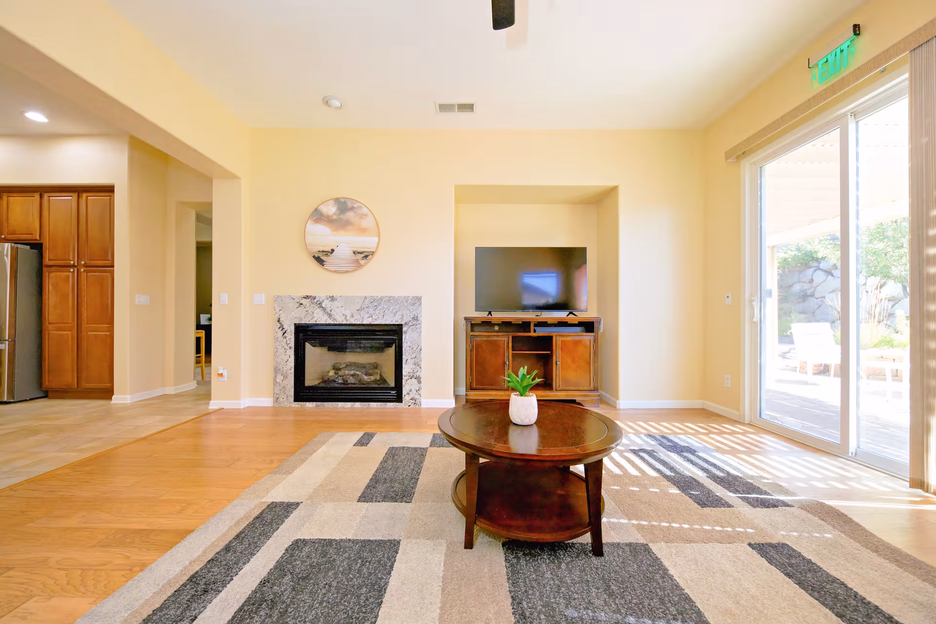 A bright living room with a fireplace, TV stand, coffee table, rug, and sliding glass doors.