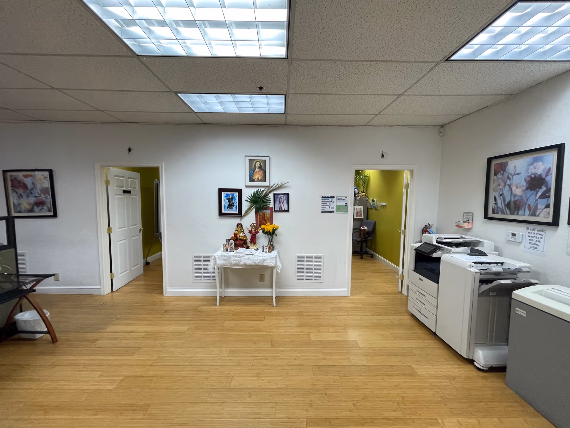 Interior common area with an altar table, religious icons, framed pictures, and office printers.