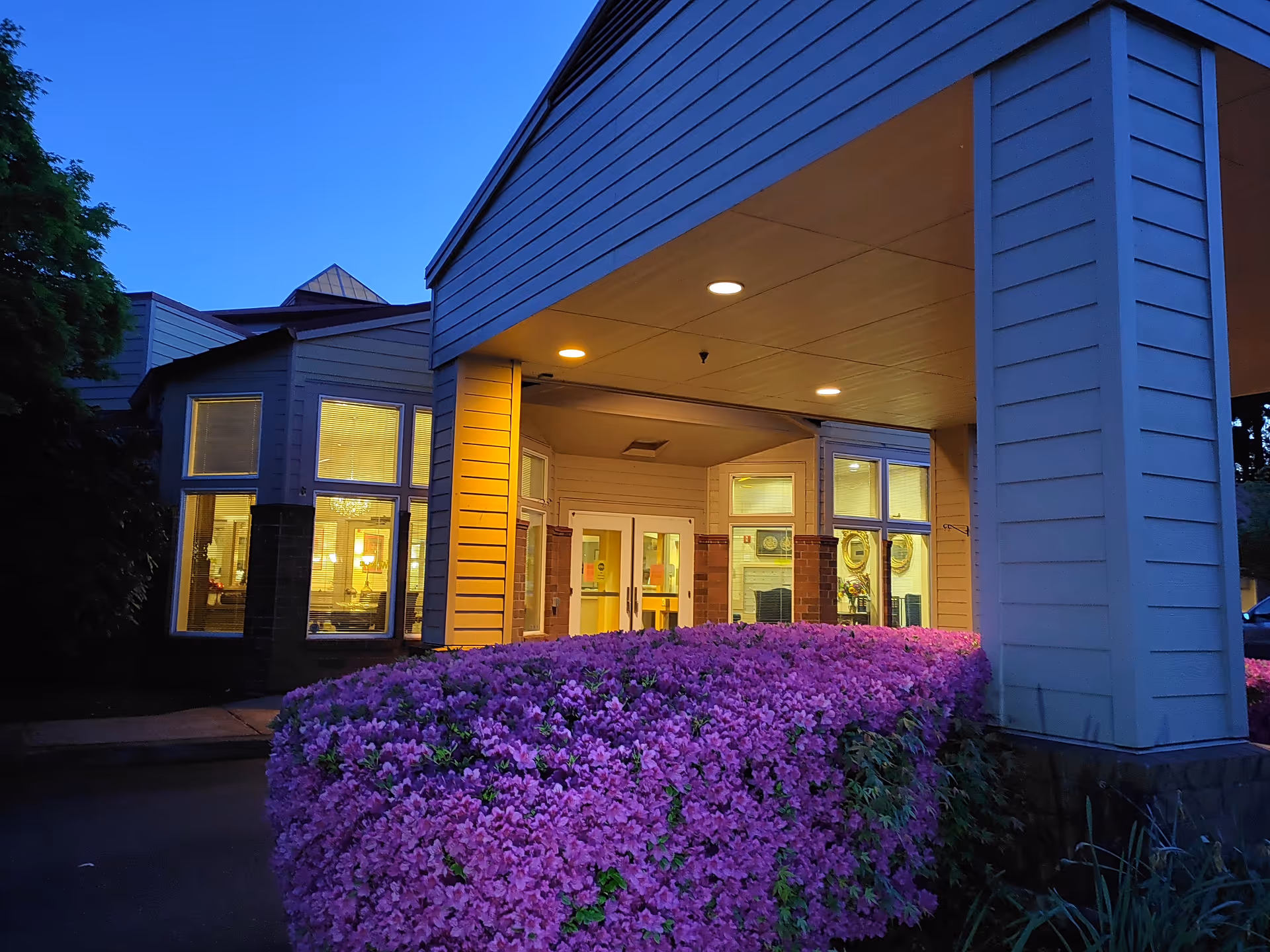 Exterior view of Elliott Residence entrance with purple flowering shrubs and lit doors.
