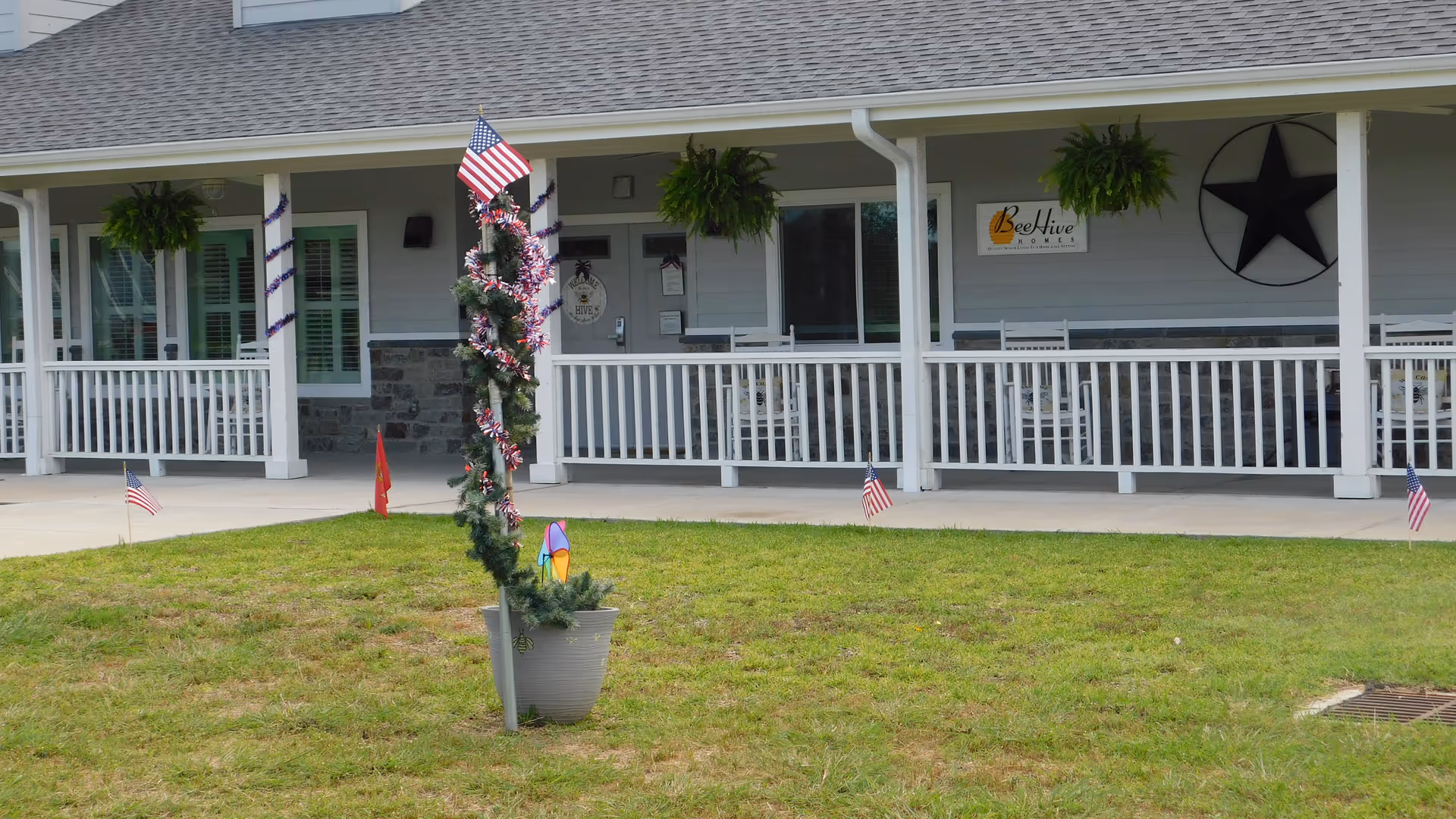Front porch of Beehive Homes Cypress Texas with hanging planters and American flags.