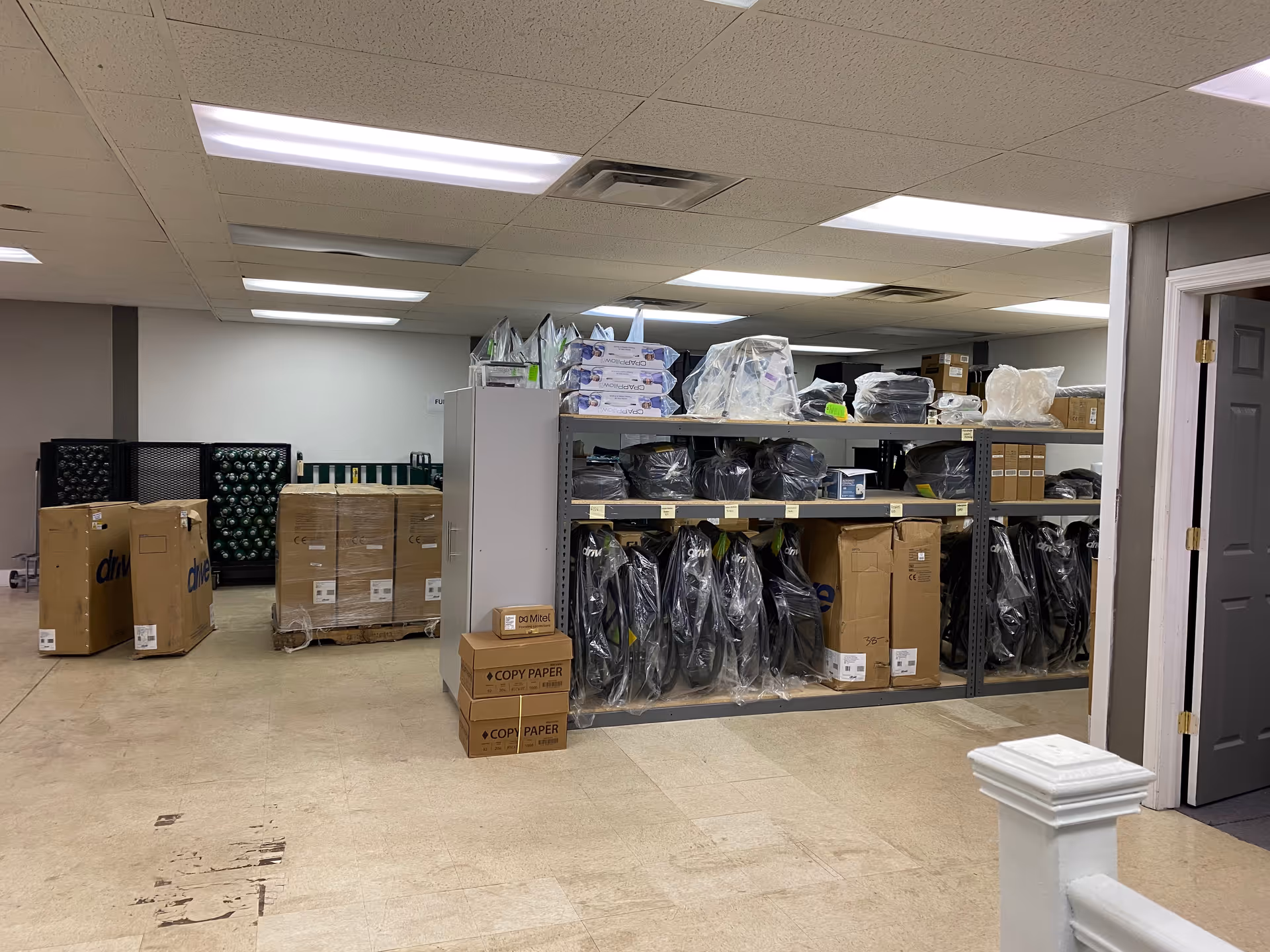 Storage area with shelves, boxes, and pallets of supplies in a utility room.