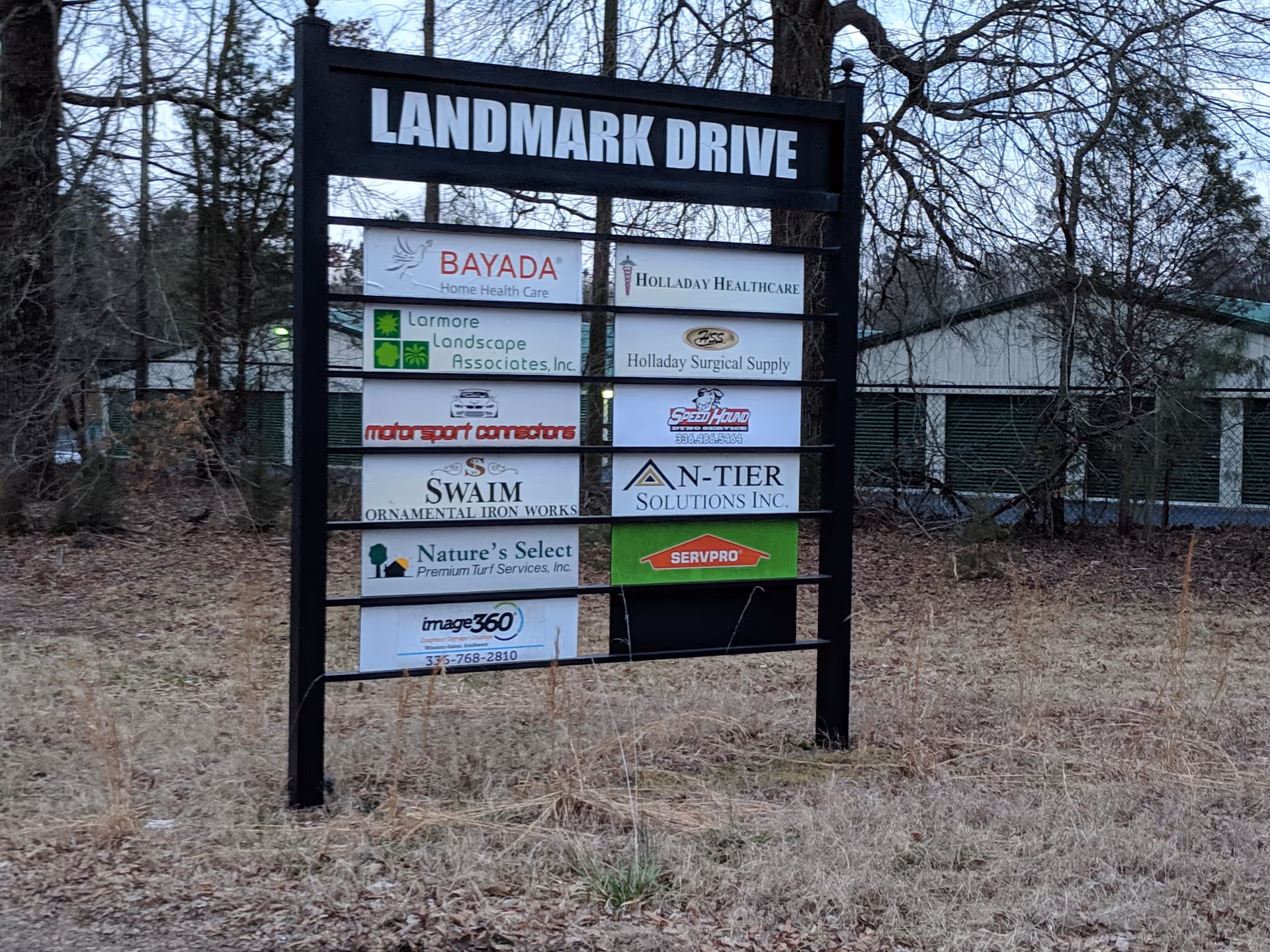 Outdoor signboard titled Landmark Drive displays Bayada Home Health and other signs in a grassy lot.
