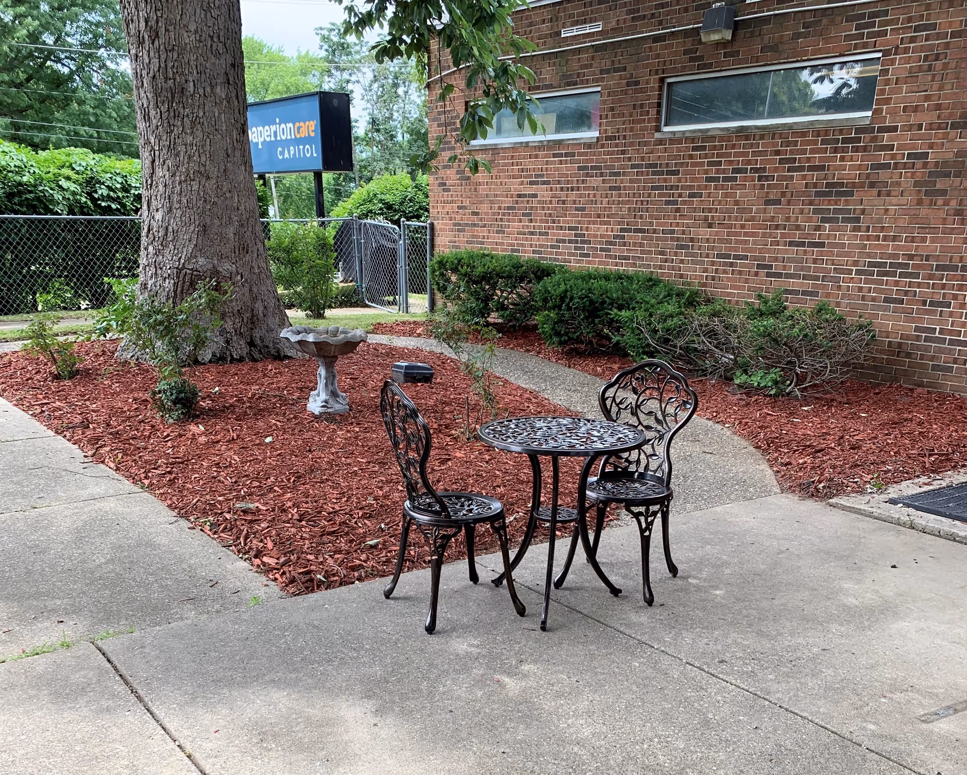 Small black wrought-iron table with matching chairs on a concrete patio beside a brick building
