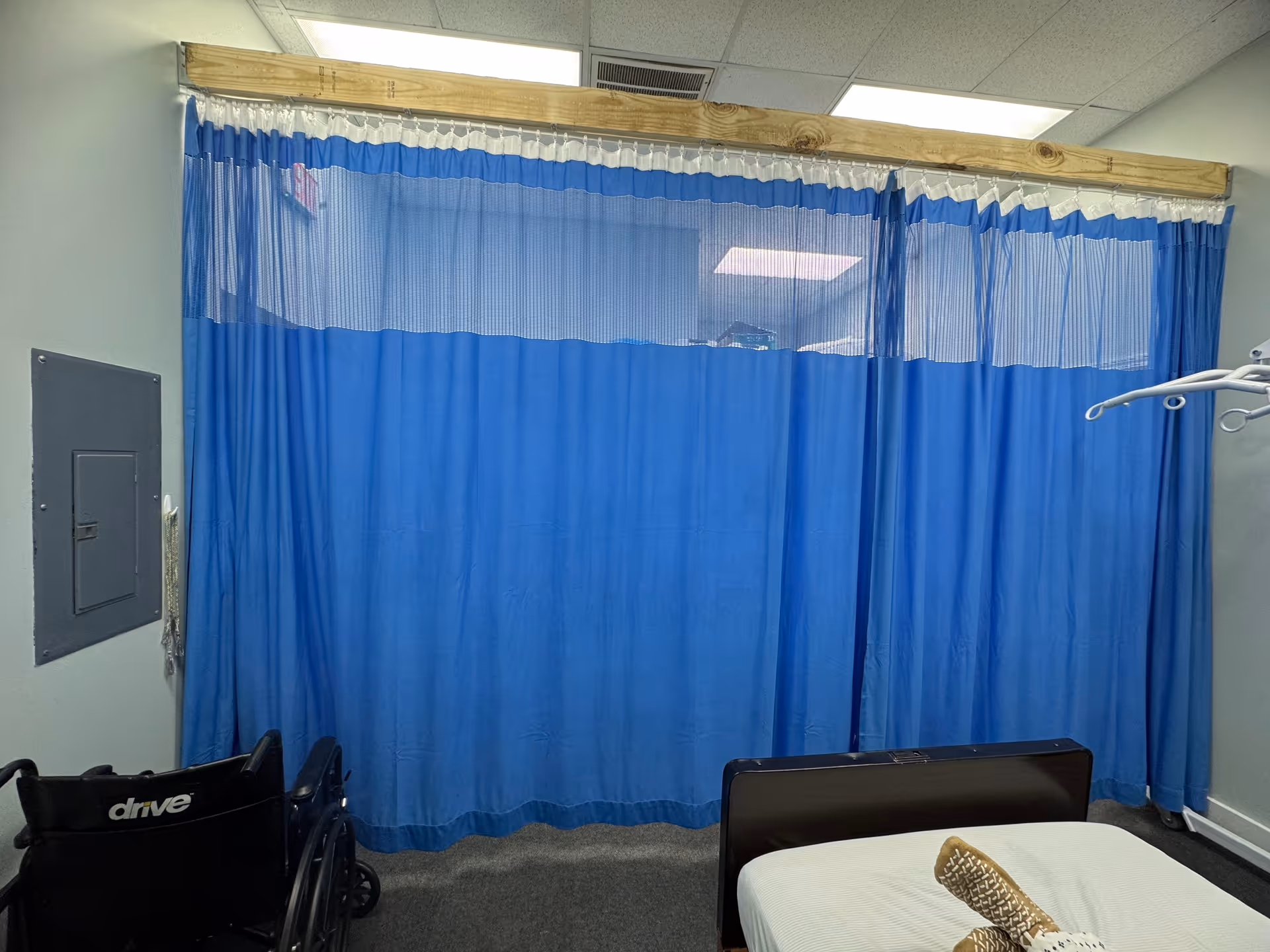 A blue privacy curtain divides a care area with a wheelchair and bed.