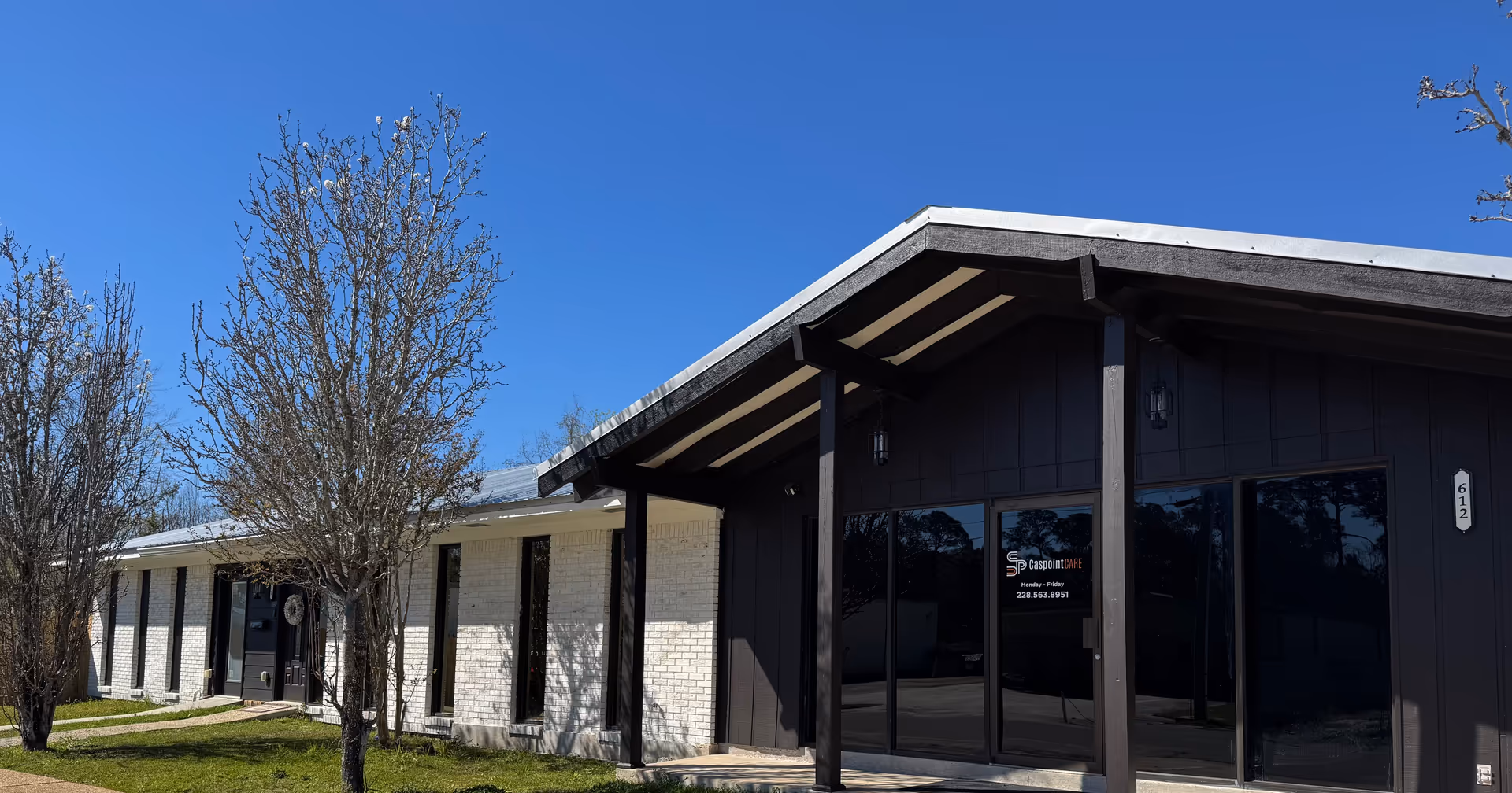 Exterior view of Caspoint Care Inc. facility with dark entrance doors and leafless trees, blue sky.