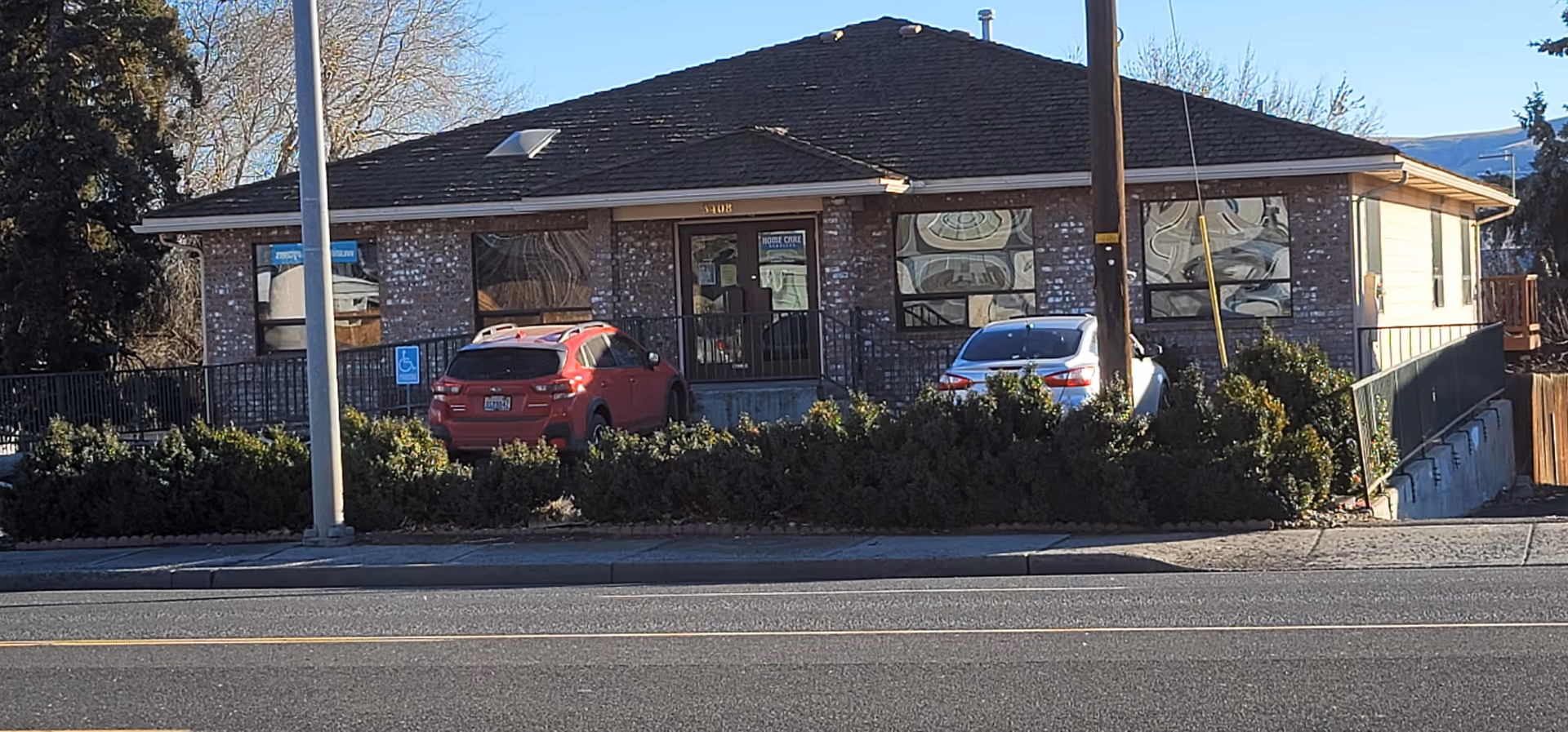 Single-story brick building labeled Home Care Services Yakima with parked cars and hedges in front