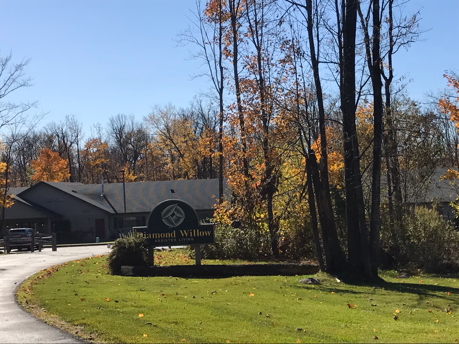 Diamond Willow Assisted Living building front with sign amid autumn trees.