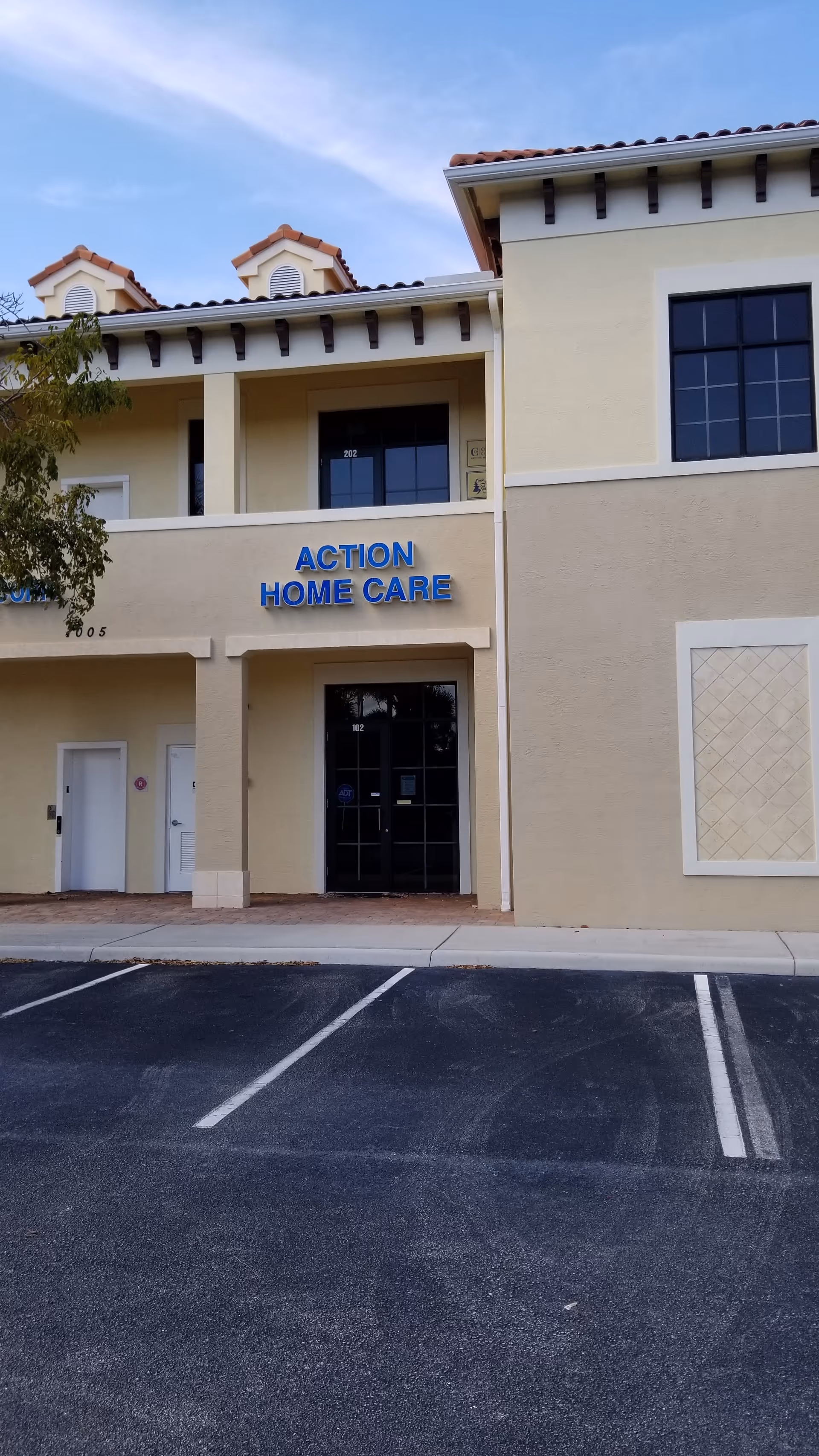 Two-story beige senior care facility with blue Action Home Care sign and parking lot.