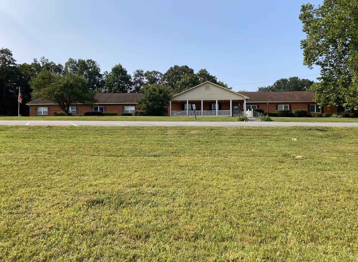 Single-story brick building with a central covered entrance, front lawn, and parking.