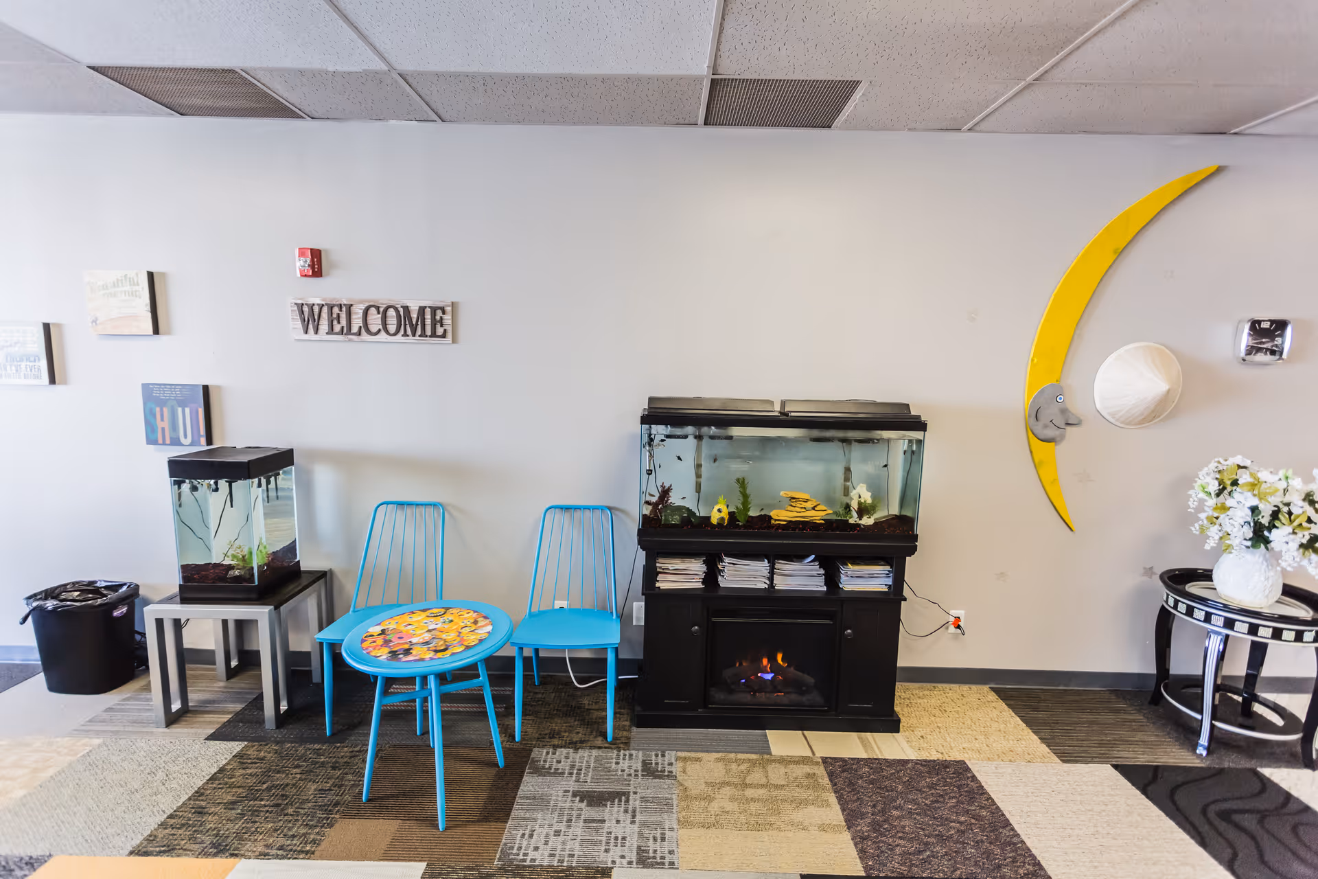 Lobby area with blue chairs, aquarium tanks, a faux fireplace, and decorations.