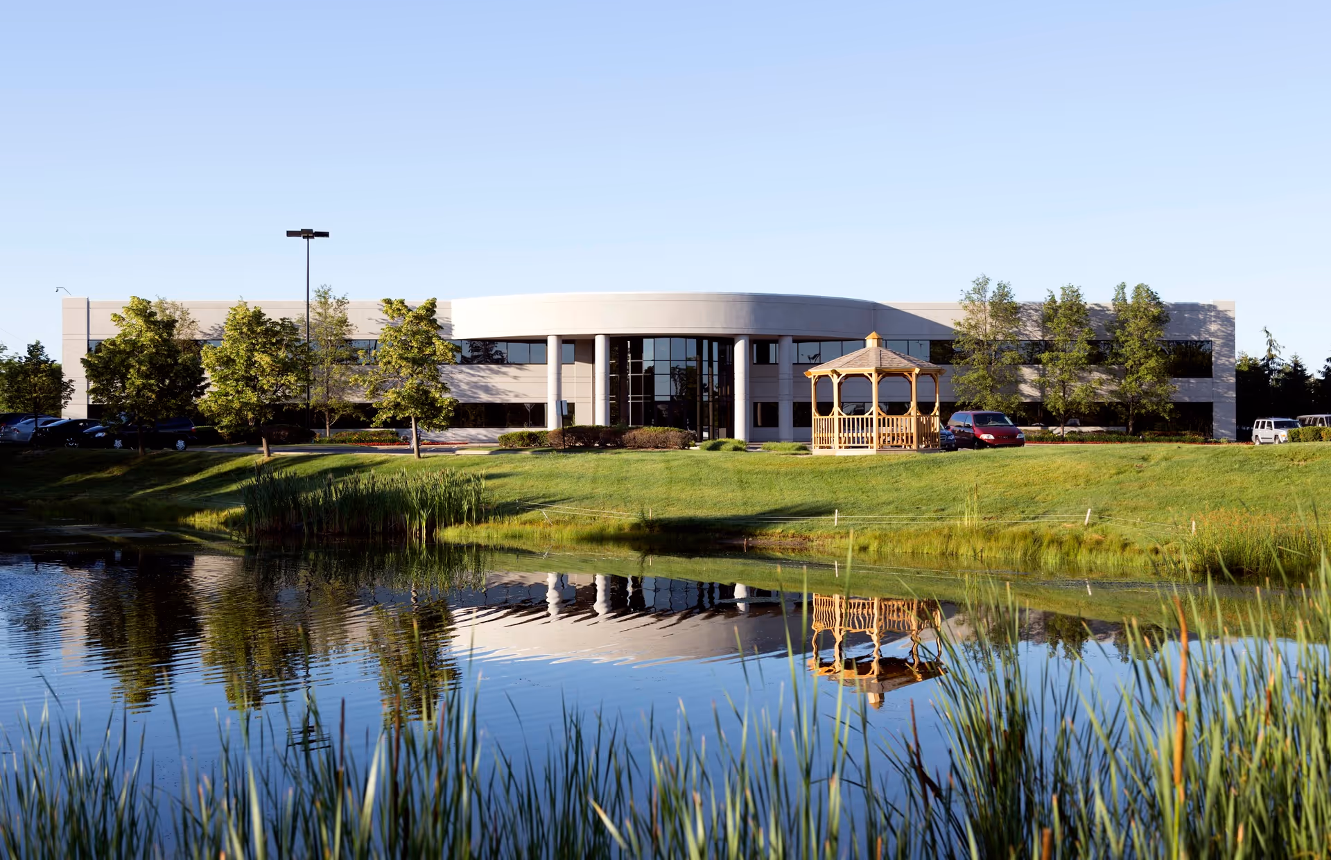 Front exterior view of a modern senior living facility with a pond and gazebo.