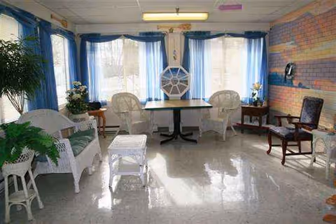 Sunlit indoor dining area with a round table, wicker chairs, and blue curtains.