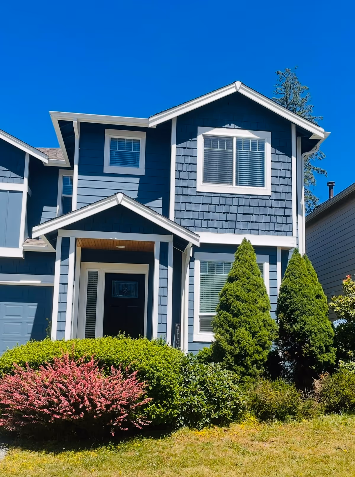 Front exterior of Blooming Life Adult Family Home: blue house with white trim and landscaped yard.