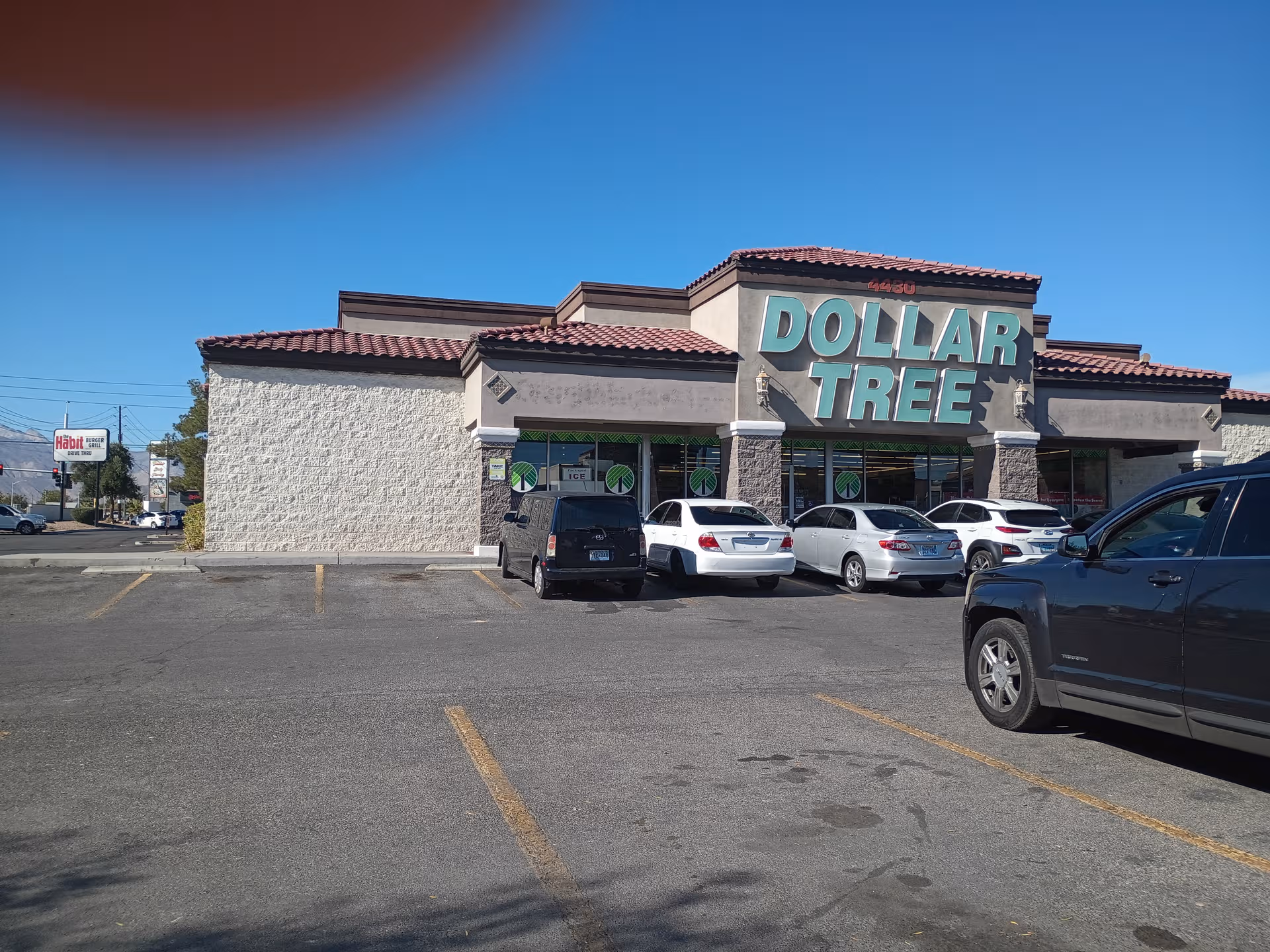 Exterior view of a Dollar Tree storefront with several parked cars under a clear blue sky.