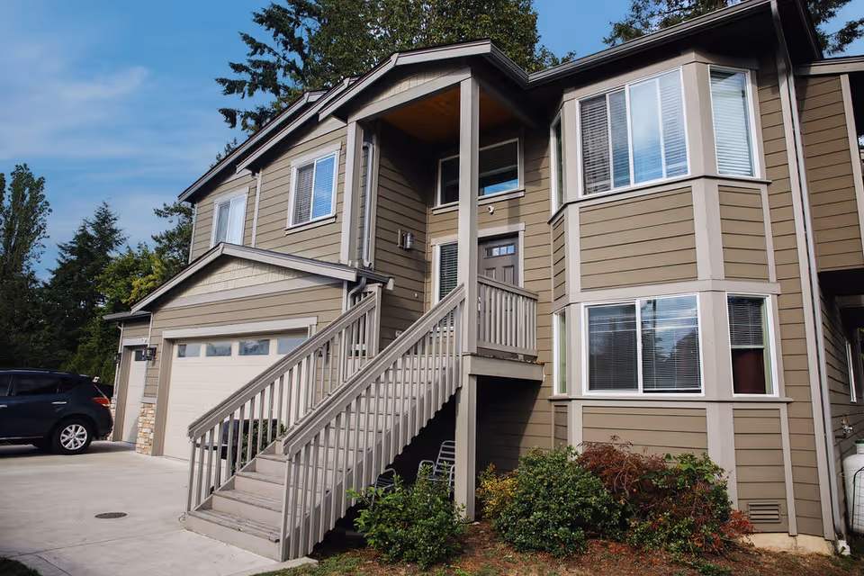 Exterior view of a tan, two-story townhouse with stairs and a garage.