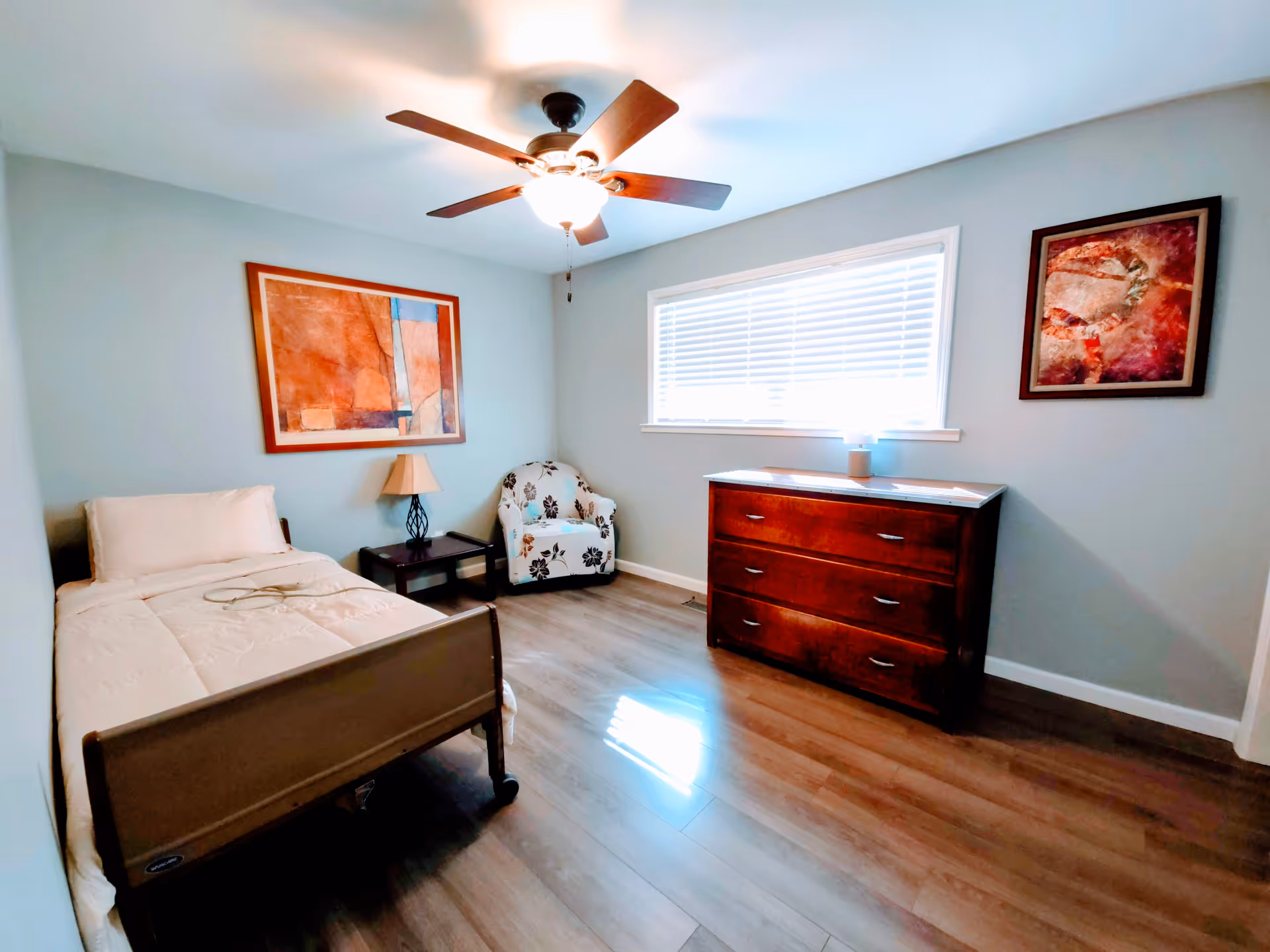 A tidy bedroom with a single bed, dresser, chair, window, and ceiling fan.