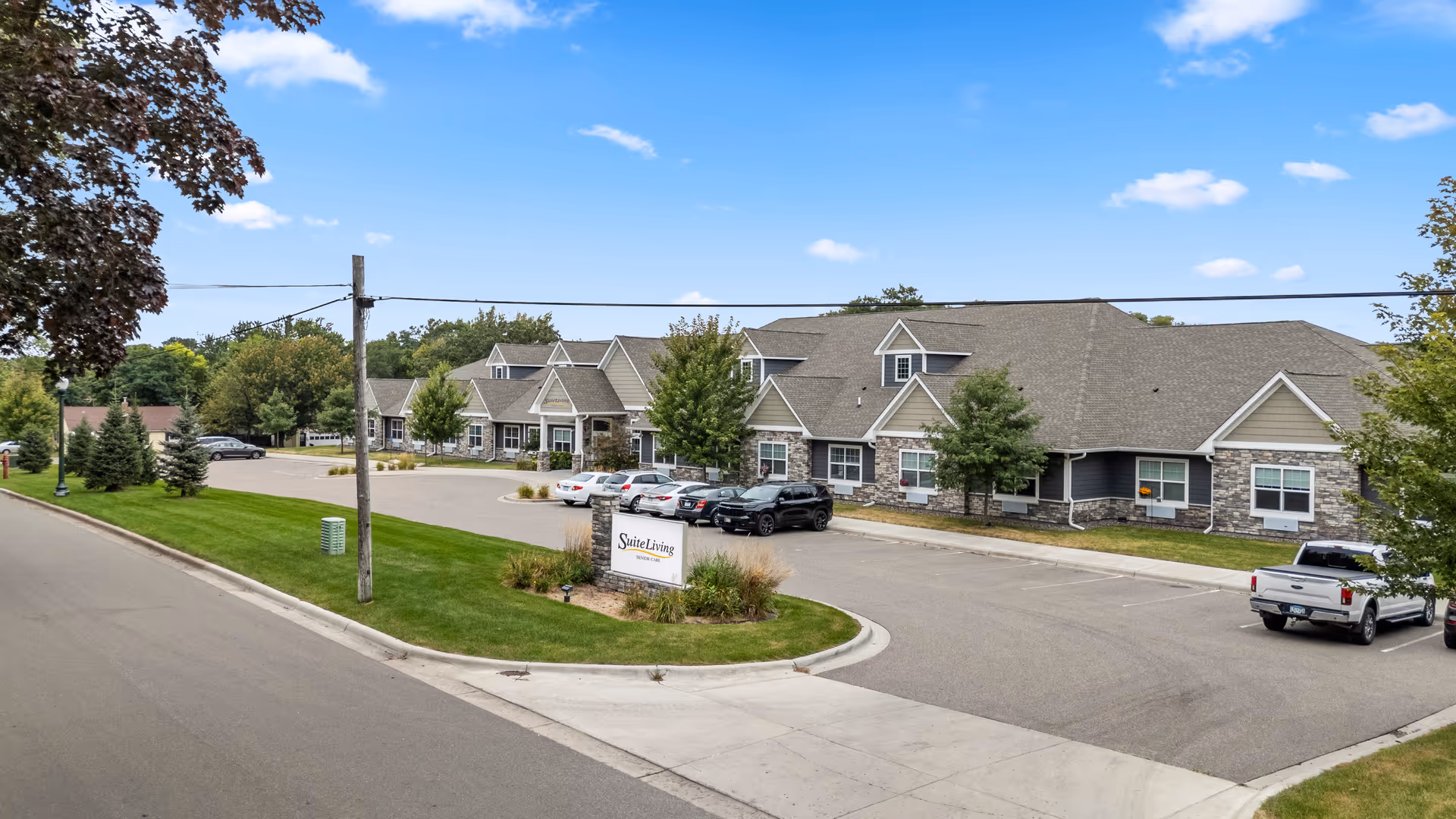Exterior view of Suite Living of Anoka facility with parked cars and landscaping.