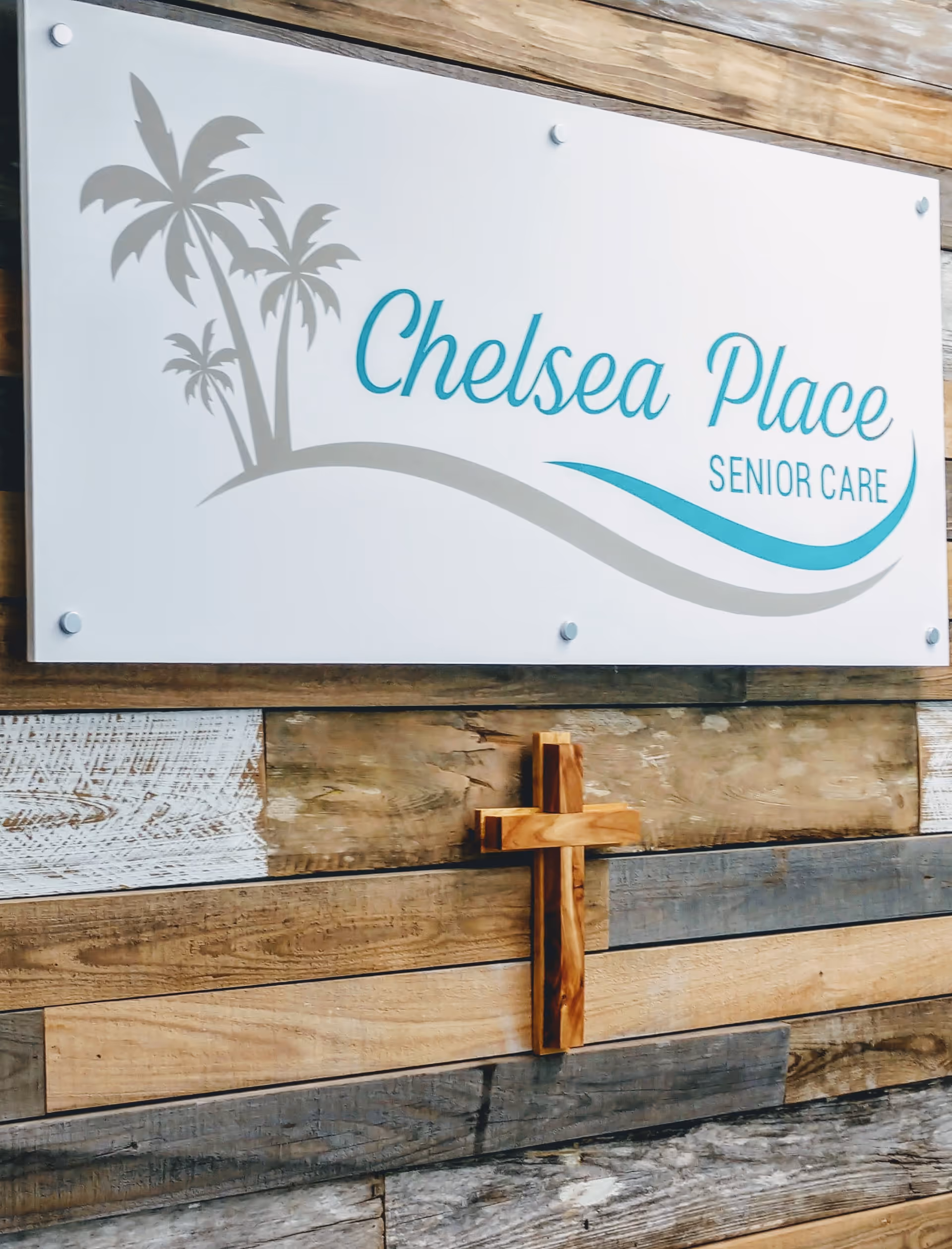 Exterior wall with Chelsea Place Senior Care sign and wooden cross mounted on wood siding.