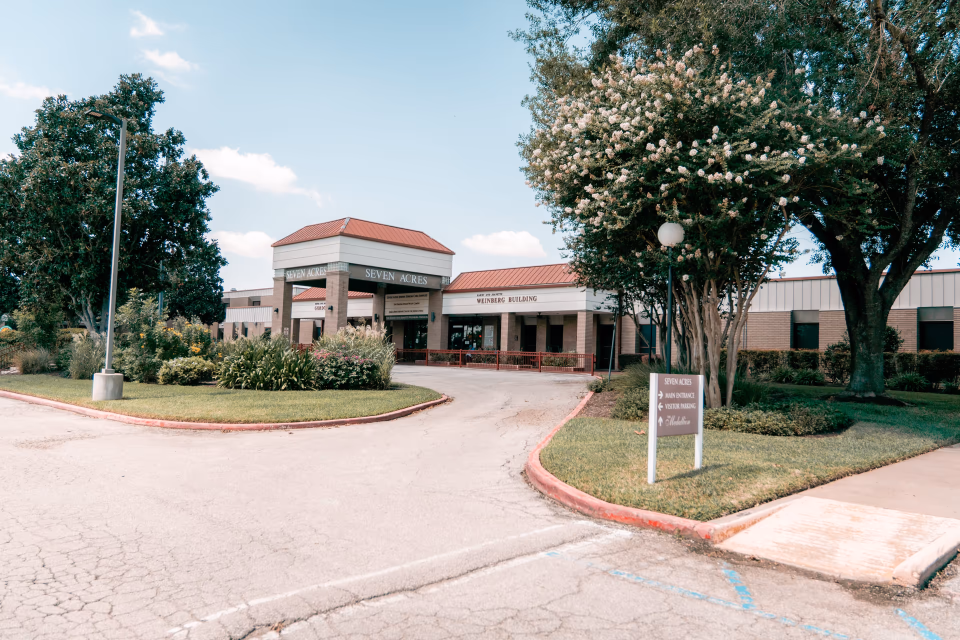 Front entrance of the Seven Acres senior care building with a circular driveway, landscaping, and trees.