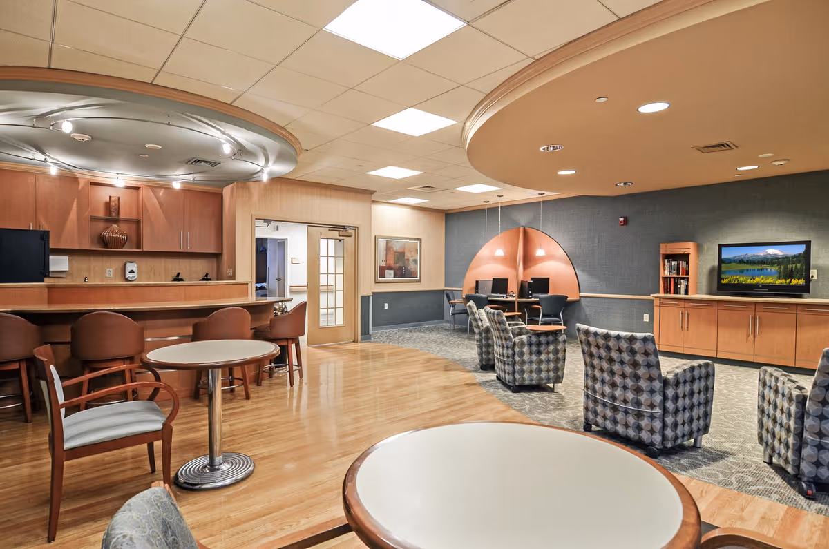 A spacious senior living common area with a curved ceiling, seating, a counter, and a TV.