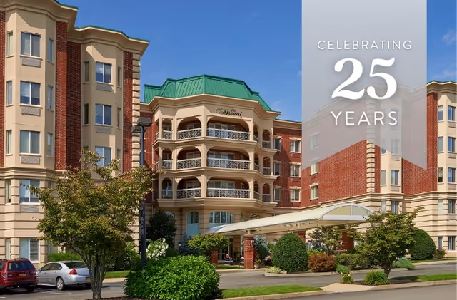 Front exterior of a multi-story senior living building with balconies, landscaping, and a vertical banner reading "CELEBRATING 25 YEARS".