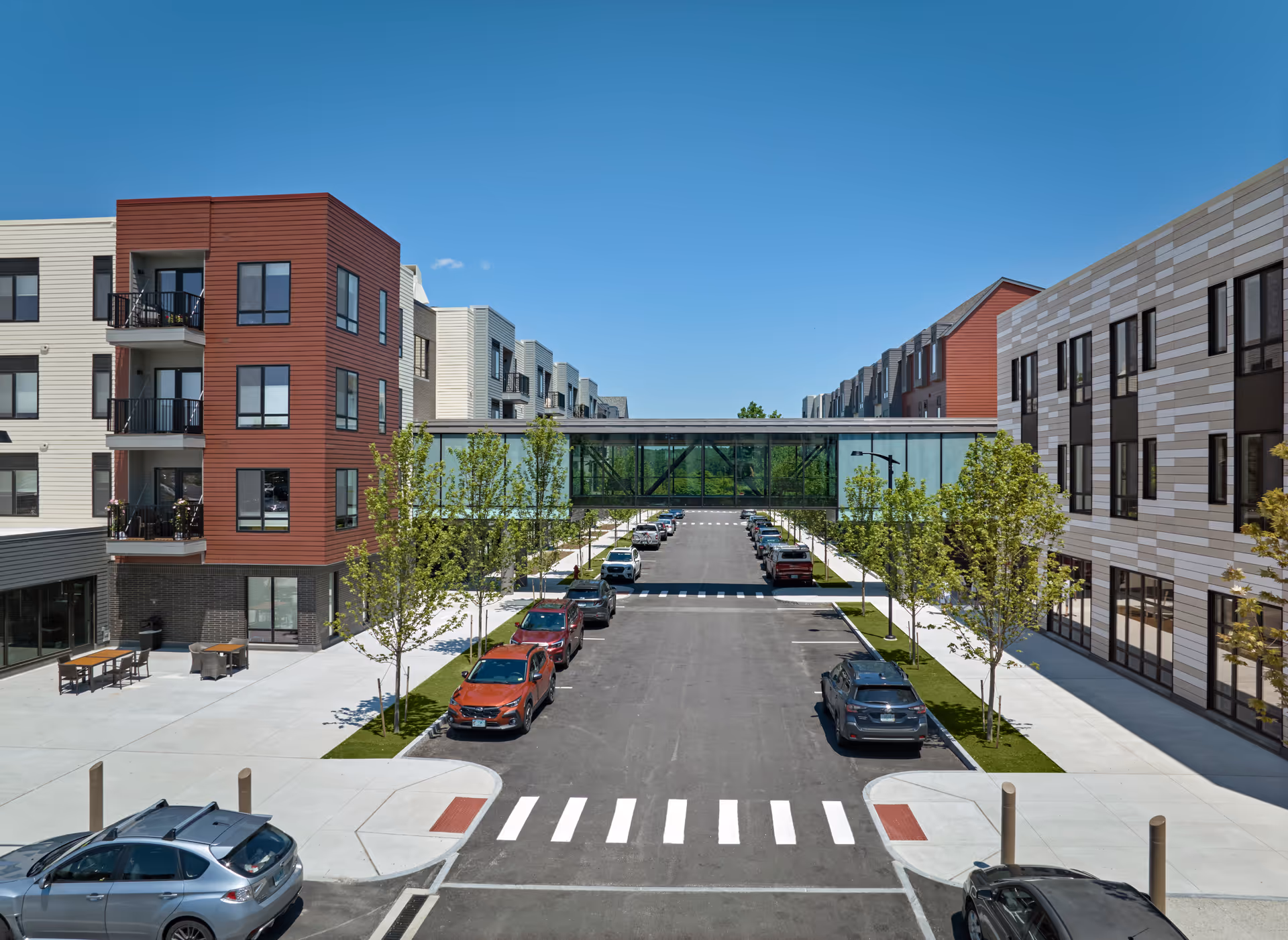 Modern senior living campus with multi-story buildings, a glass connecting bridge, and parked cars.