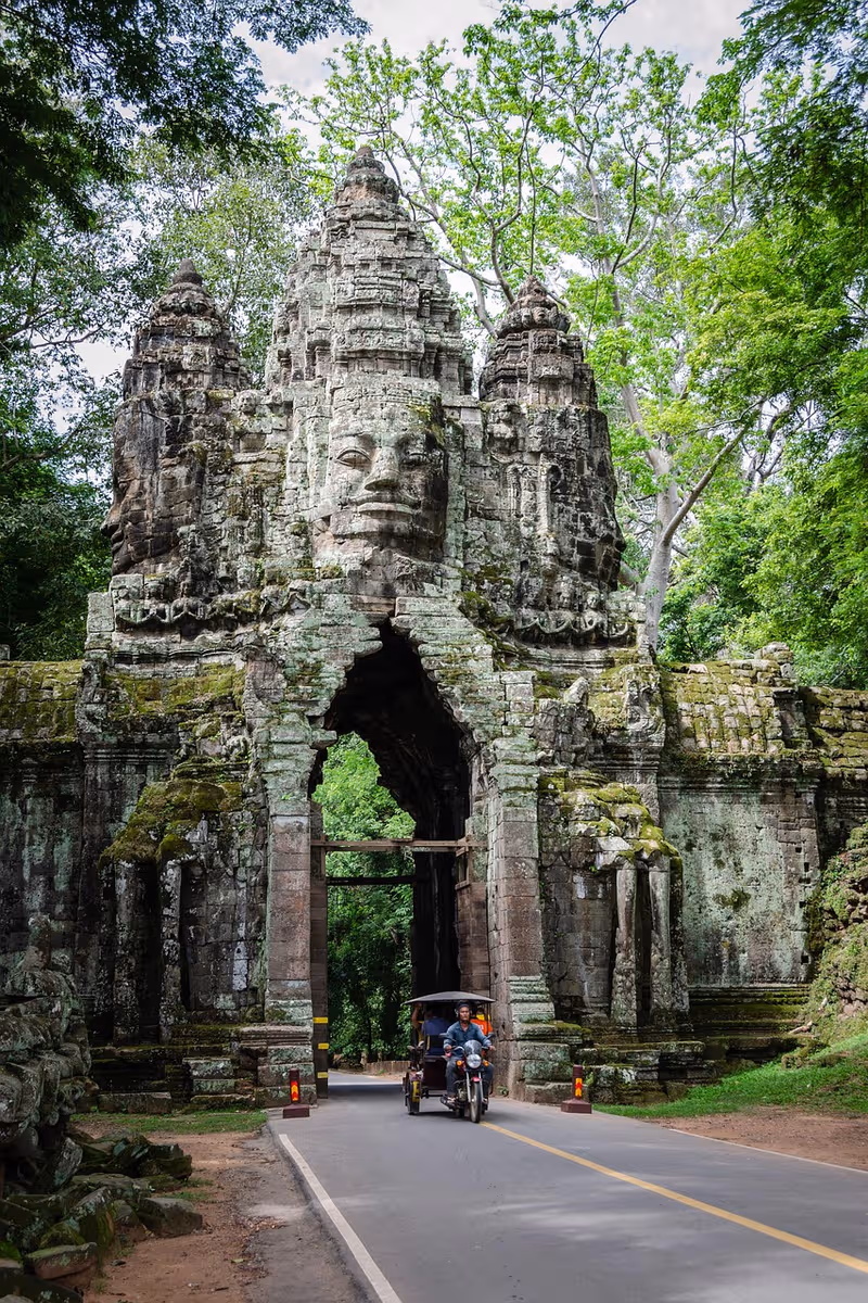 Ancient stone temple gate surrounded by lush green trees with a tuk-tuk under an umbrella