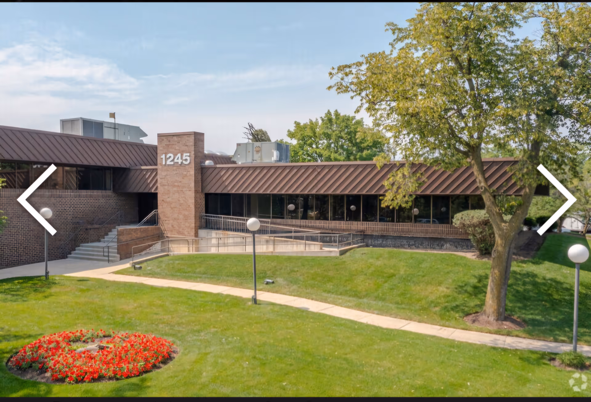 Exterior view of a brick facility with lawn, trees, and walkway toward the entrance.