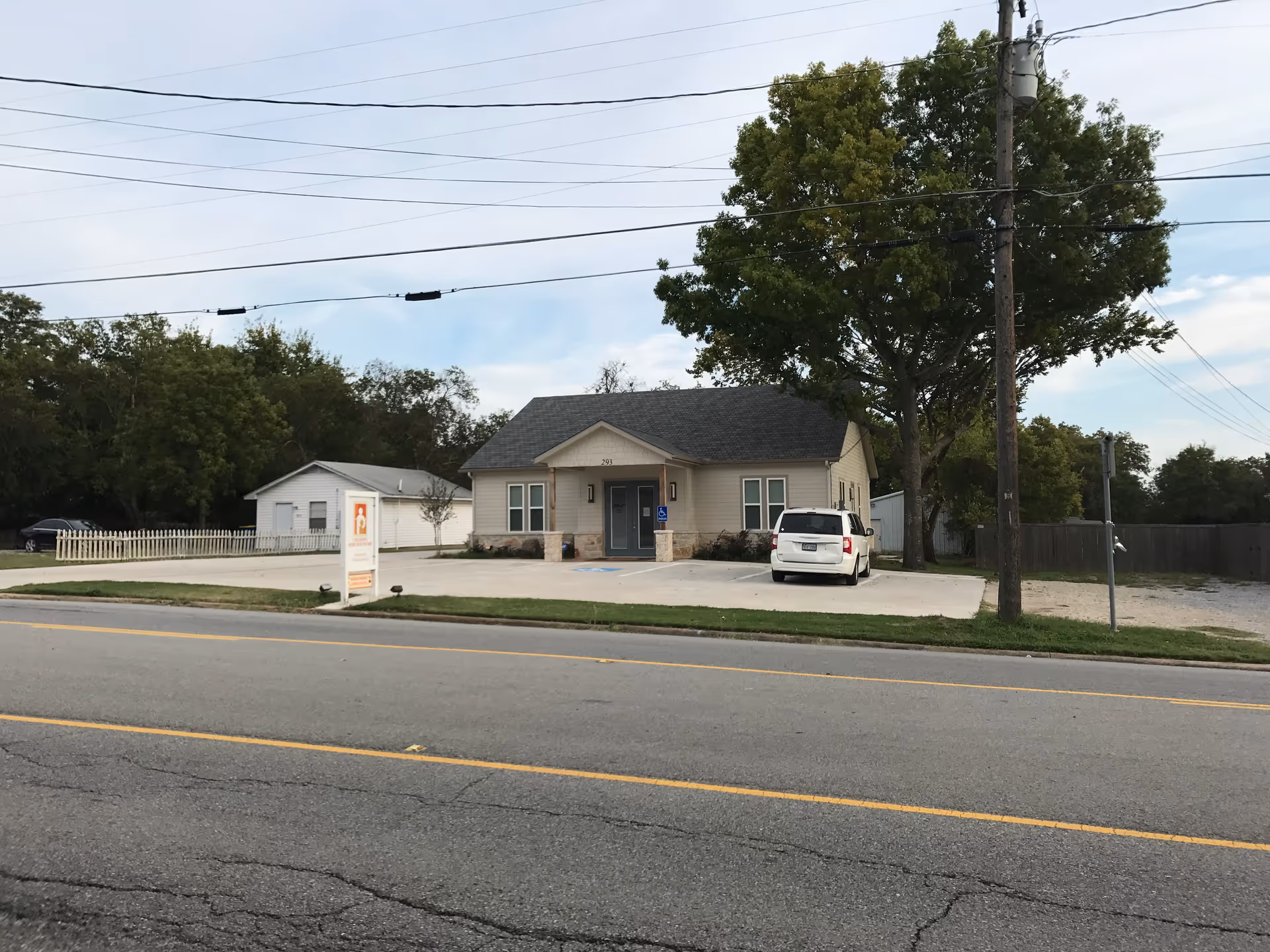 Exterior view of a single-story facility with a parking lot and a sign near the road.