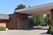 Brick Dooley Center entrance with a glass doorway under a covered canopy, a paved driveway, and trees surrounding the building.