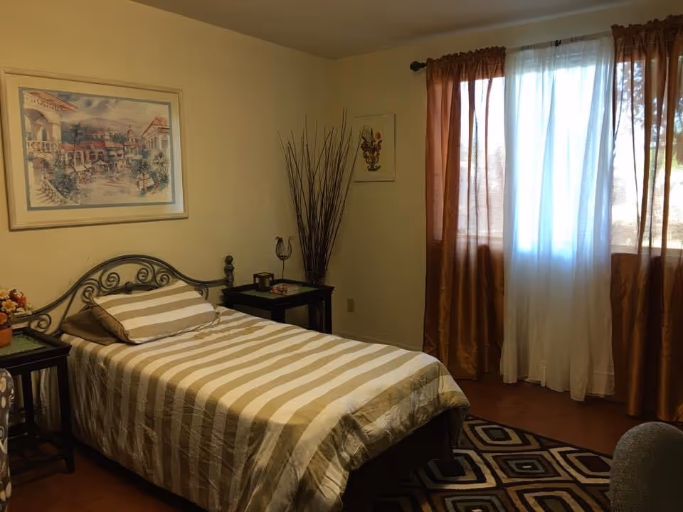 Cozy bedroom with striped bed, two nightstands, art, and sheer curtains.