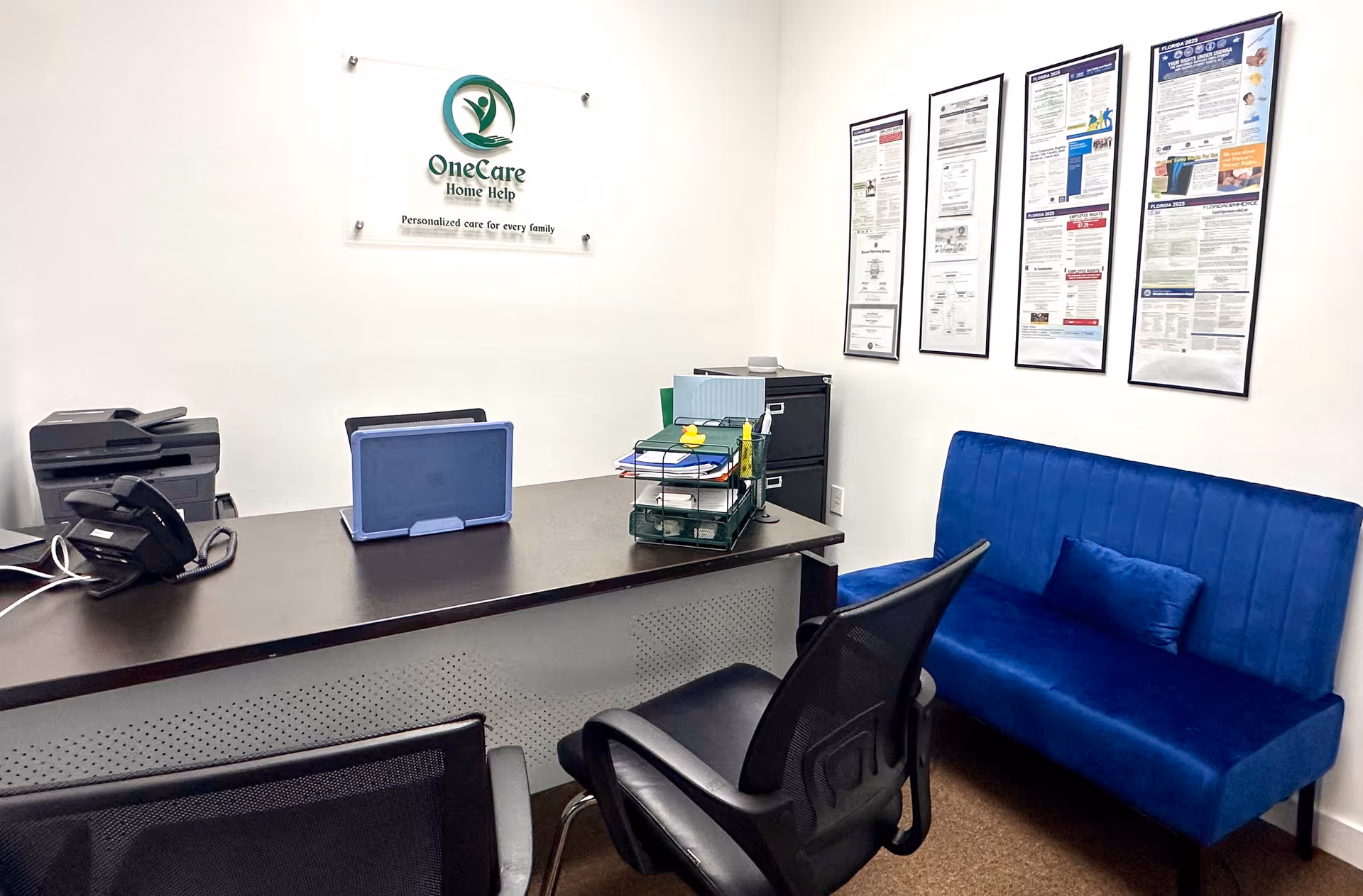 Reception area of OneCare Home Help INC with desk, blue sofa, and posters.