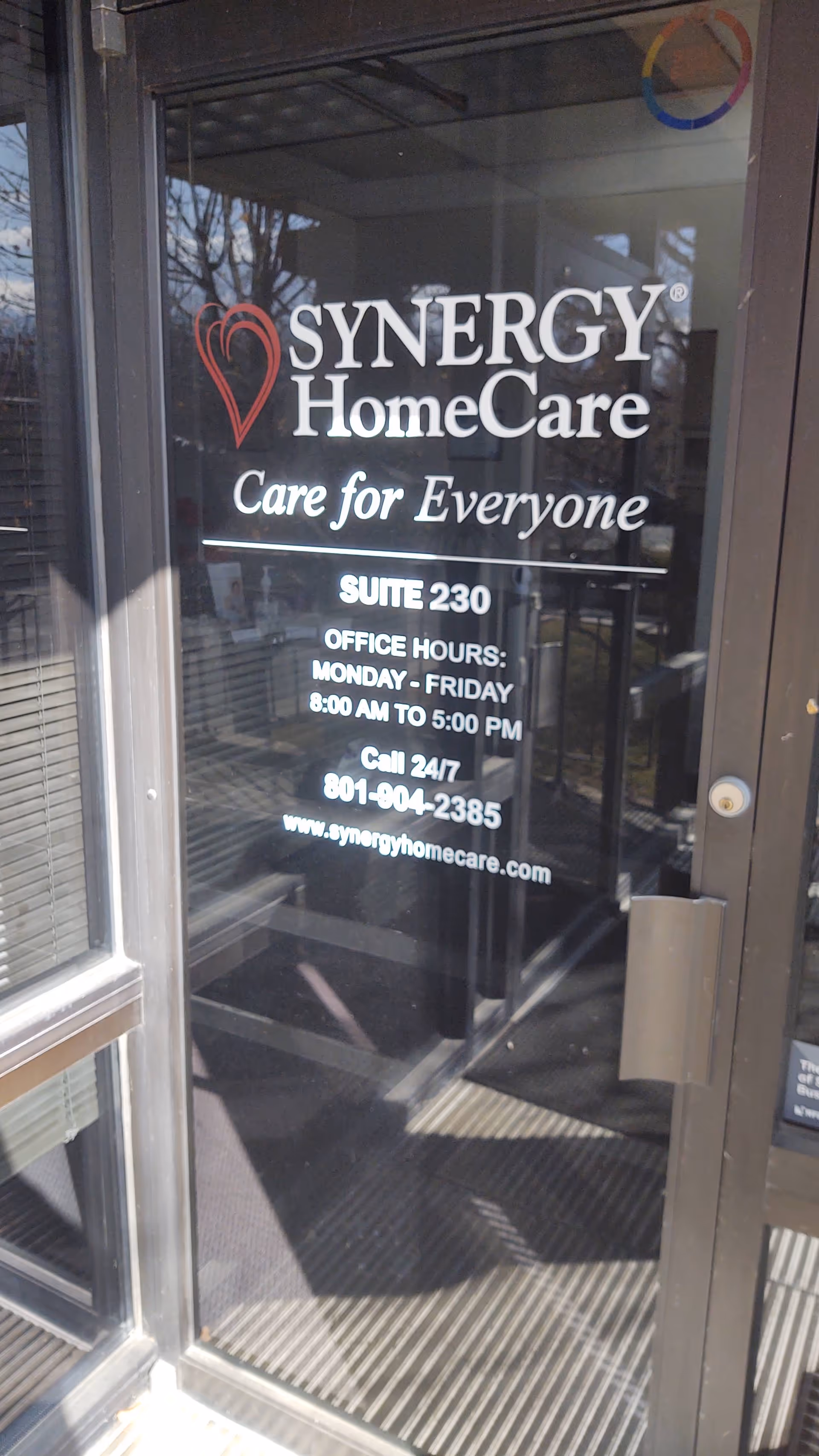 Glass door entrance with Synergy HomeCare logo and office hours displayed.