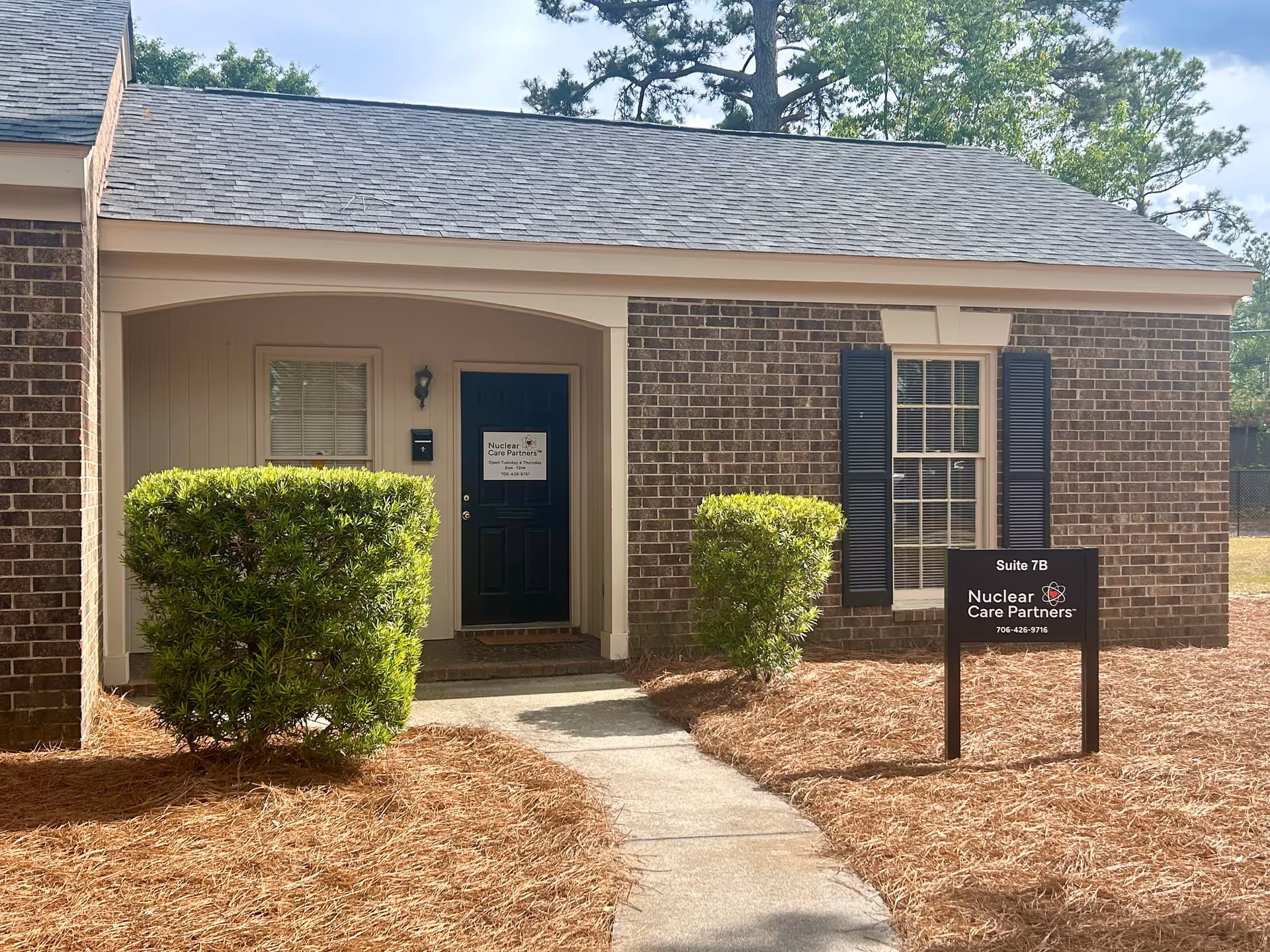 Brick single-story building with a dark door, shrubs, and a sign reading Nuclear Care Partners.