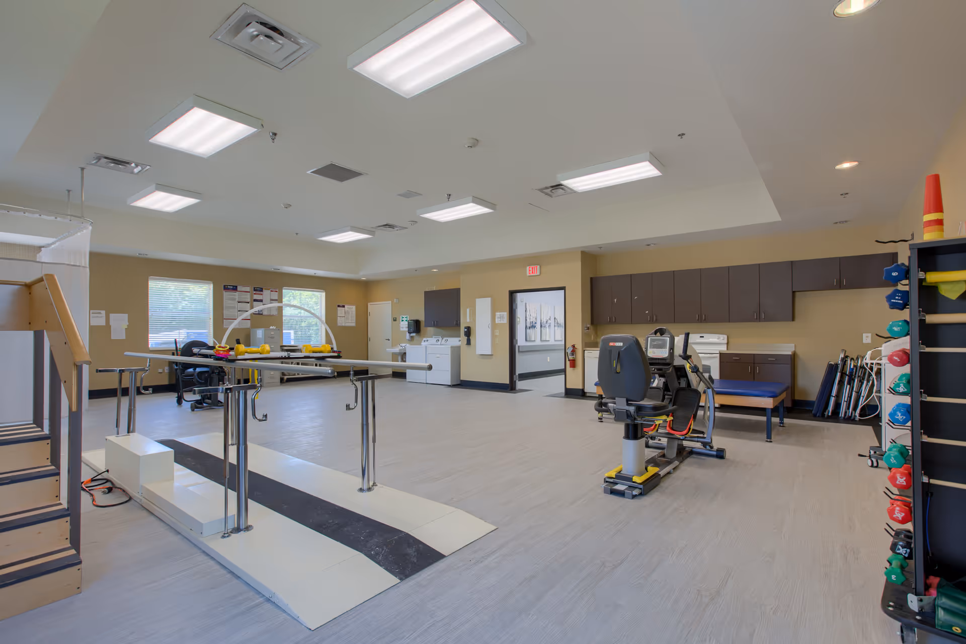 Bright rehabilitation gym at Brentwood Place Two with exercise machines and parallel bars.