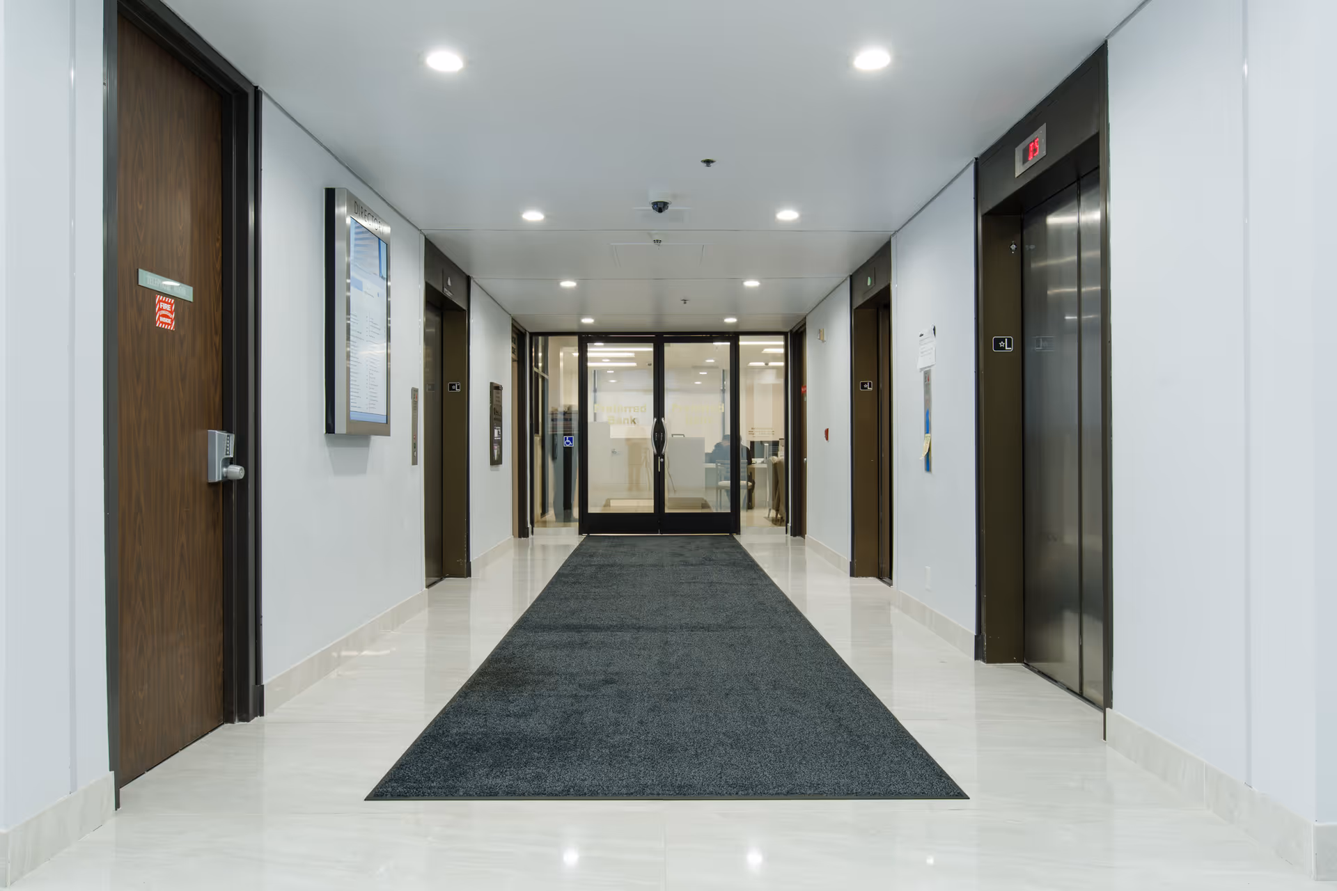 Bright hallway inside a senior living facility with multiple doors, glass entrance, and an elevator.