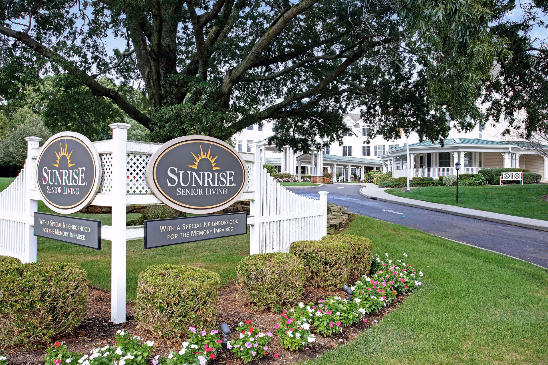 Entrance sign and landscaped front driveway of the Sunrise Senior Living facility with the building and covered portico in the background.