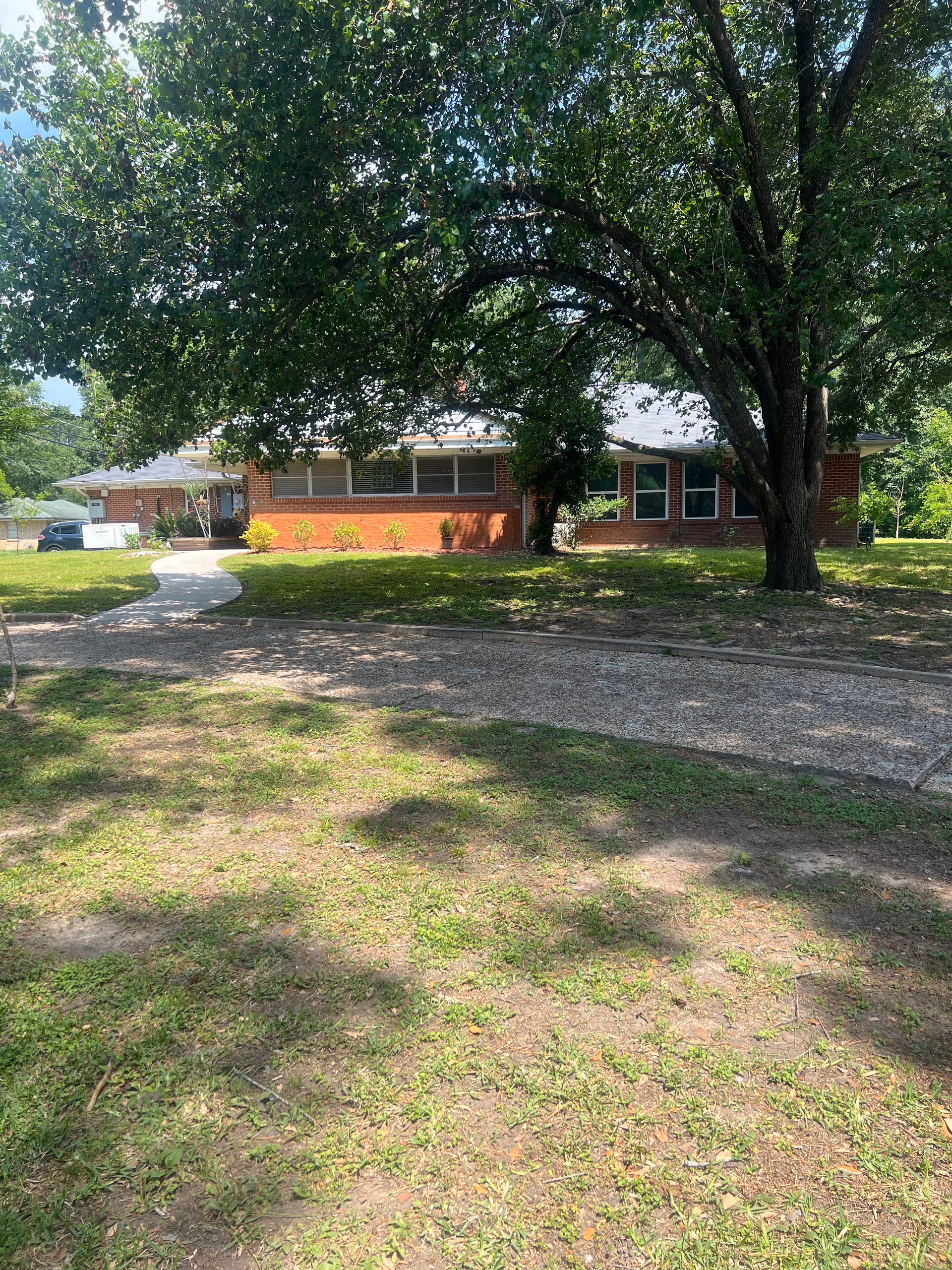 Single-story brick assisted living facility with a large tree and green lawn in front.