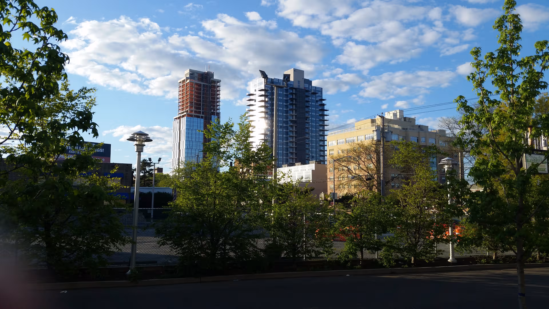 Urban cityscape with trees, street lamps, and modern buildings under a blue sky.
