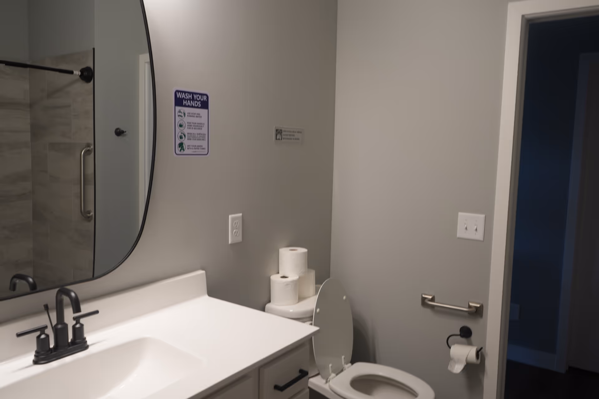 Bathroom in a senior living facility with sink, mirror, toilet, and hand-wash sign.