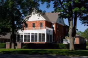 Brick two-story building with a glass-enclosed front porch and surrounding trees.