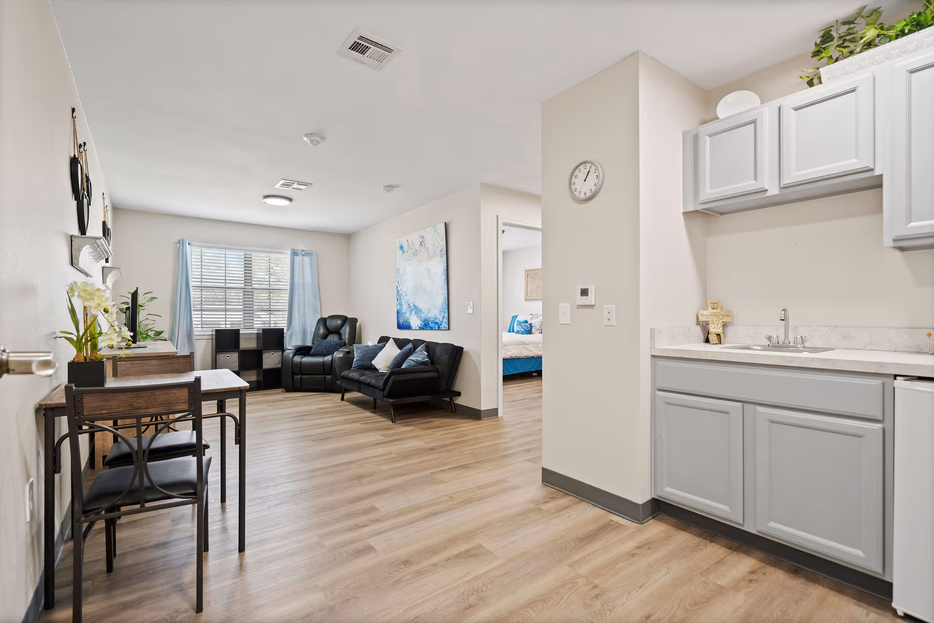 Open-concept living area with kitchenette, dining table, and seating, leading to a bedroom.