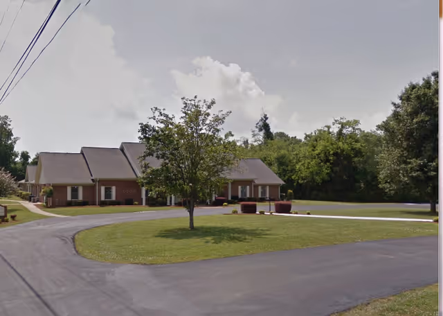Exterior view of a brick senior living facility with a circular driveway and manicured lawn.
