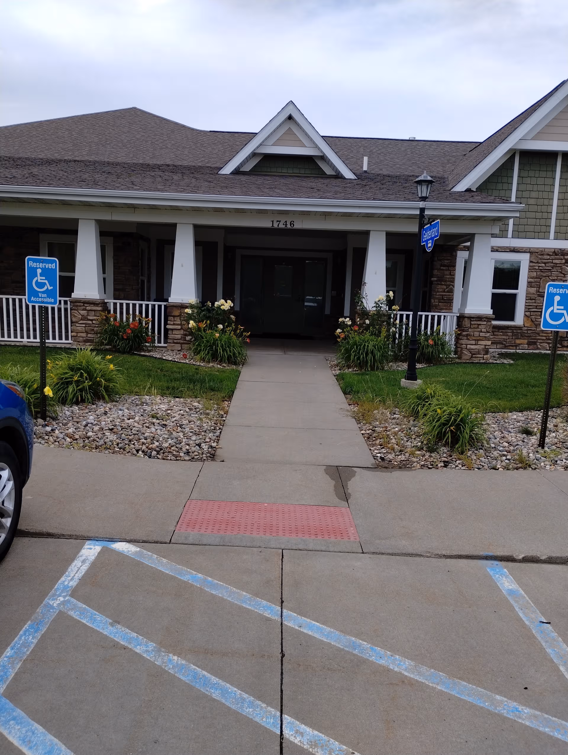 Front entrance of Hearthstone Pella senior living with handicap parking signs and landscaping.