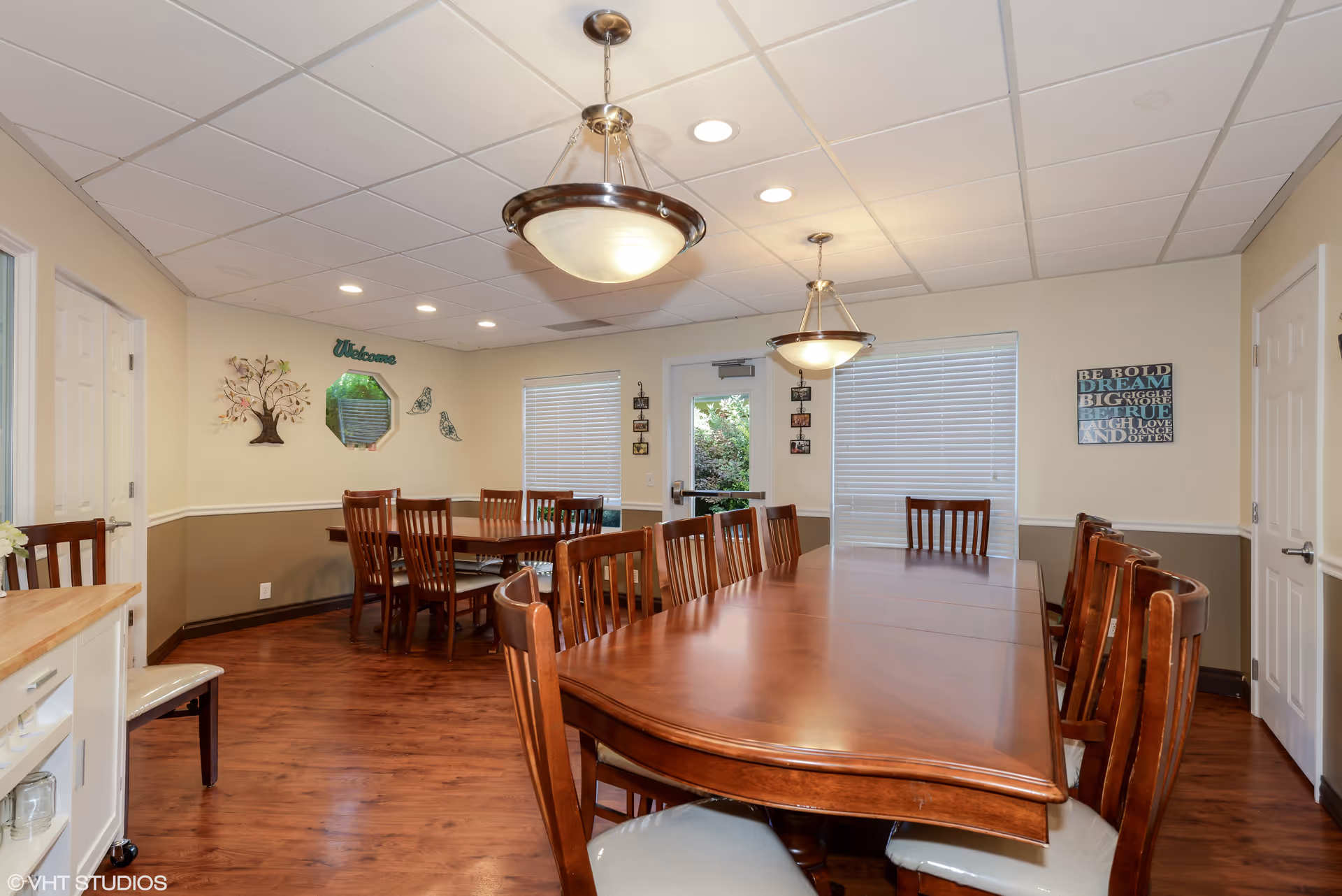 Warm dining room with a large wooden table and multiple chairs in a senior living facility.