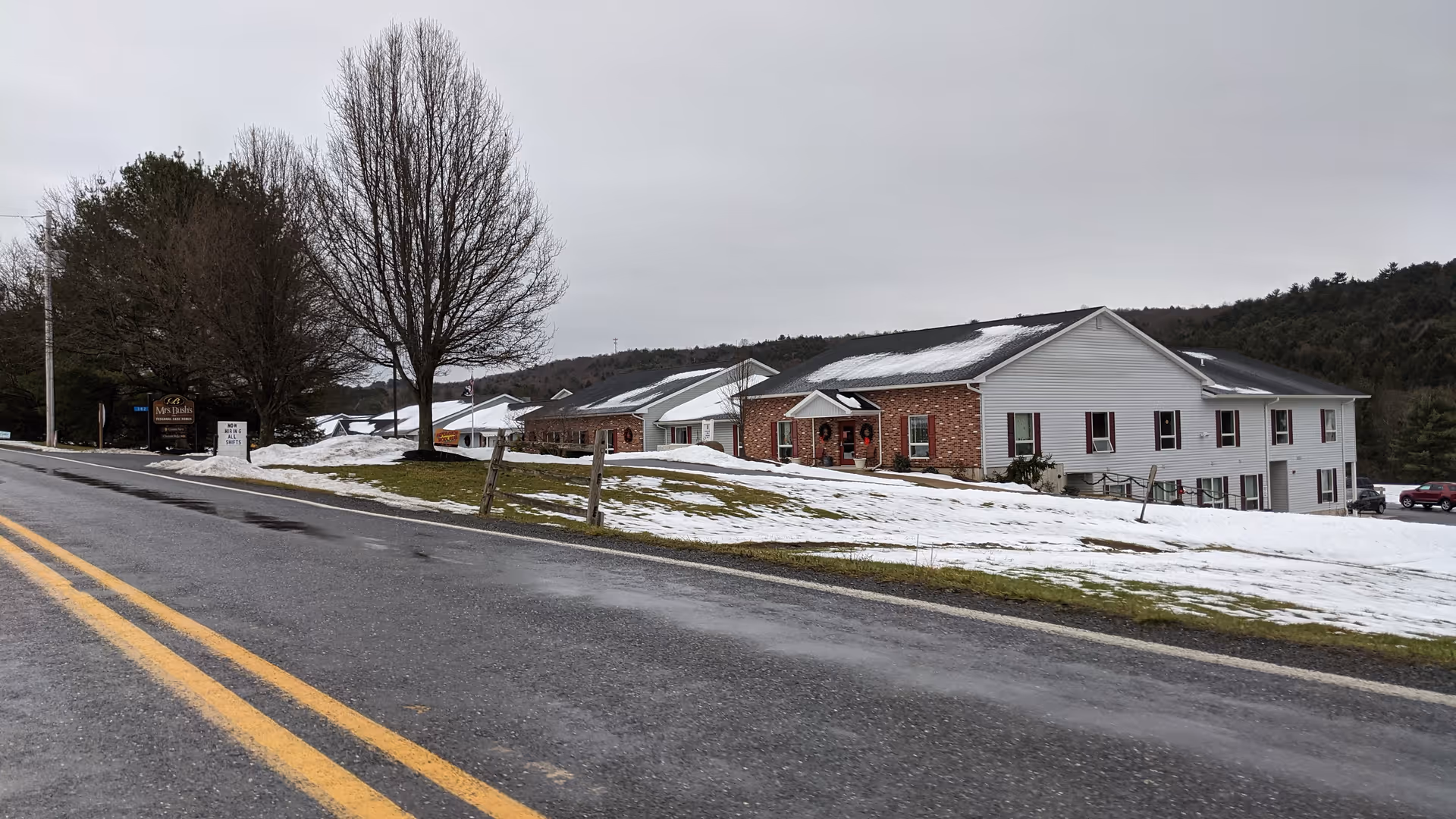 Snowy street view of a senior care home complex with brick and white siding buildings.