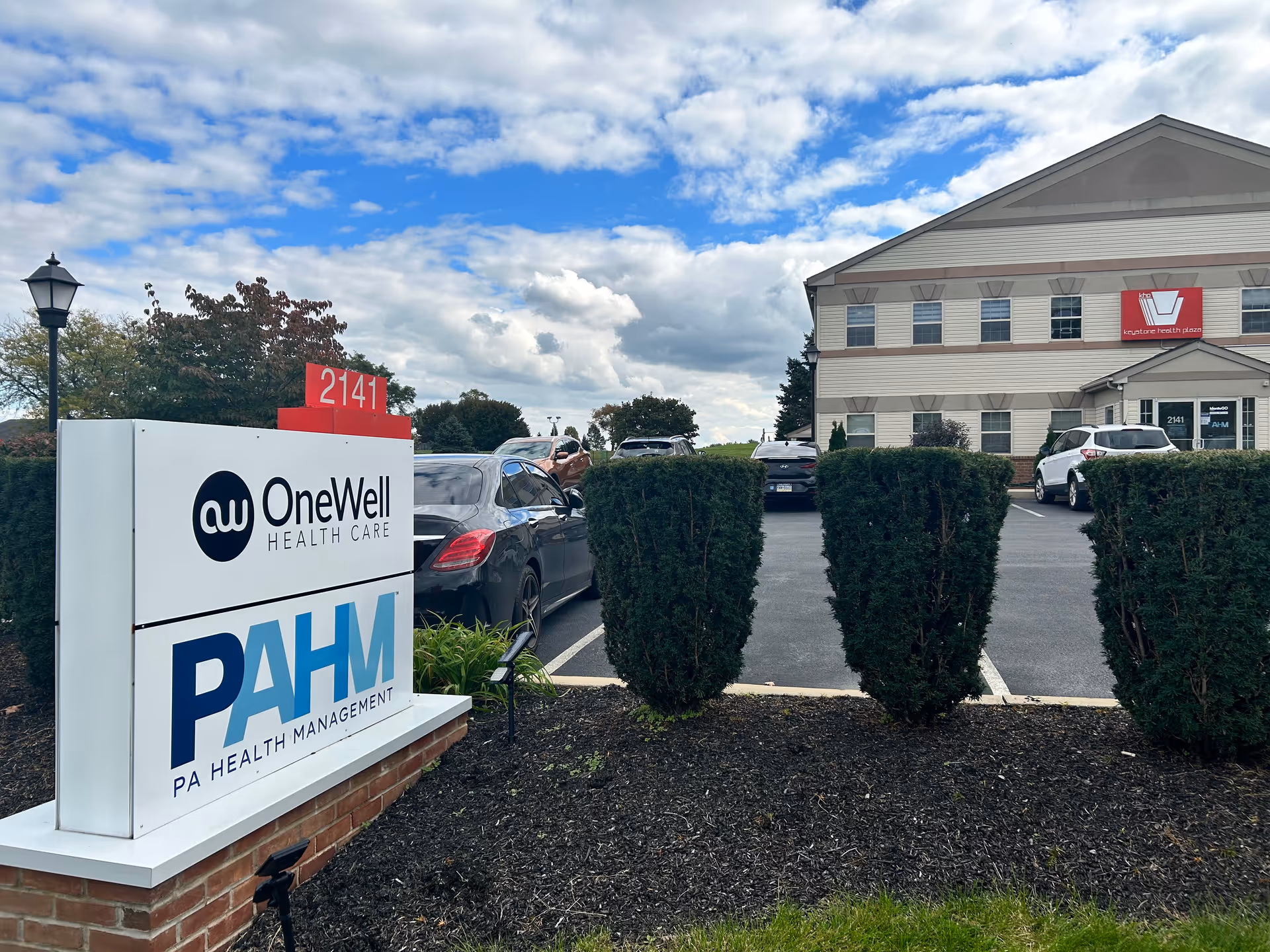 Exterior view of OneWell Health Care facility with sign, driveway, and parked cars.
