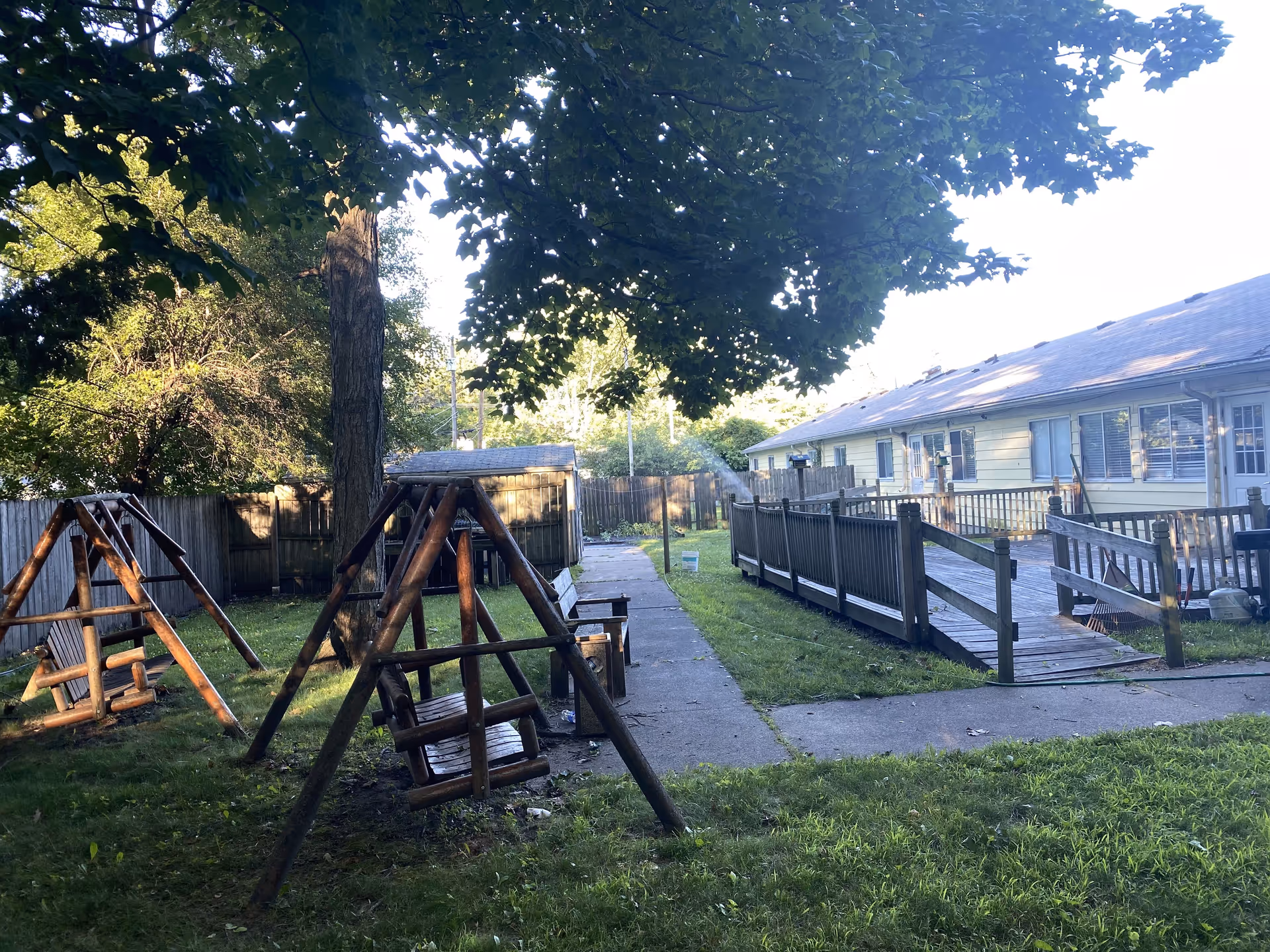 Outdoor yard of a senior facility with swings, a path, and a ramped building.
